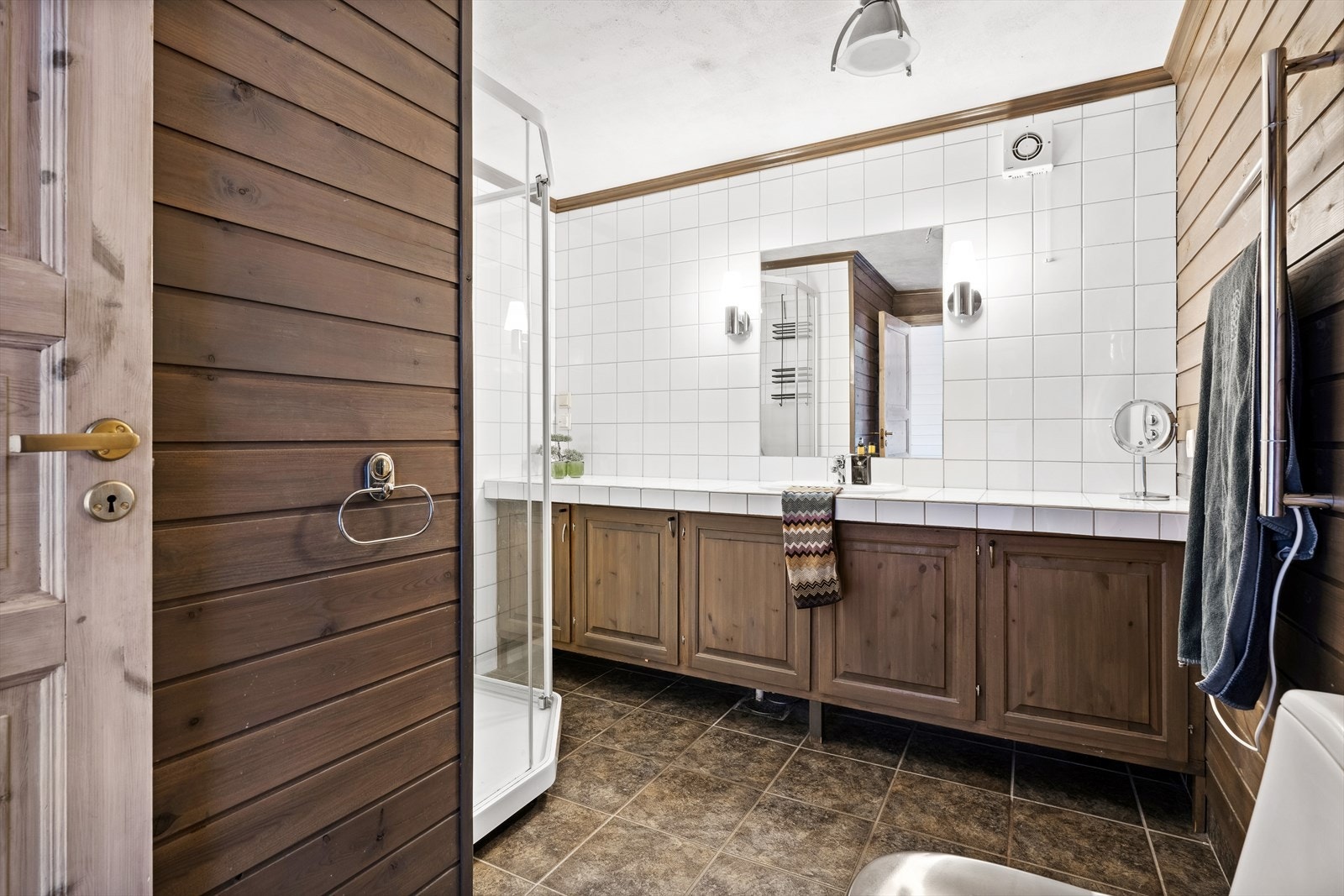 Rommet er innredet med nedfelt servant på innredning med skap, speil, toalett og dusjkabinett.
Badet har avtrekk via elektrisk styrt vifte. Galleribilde