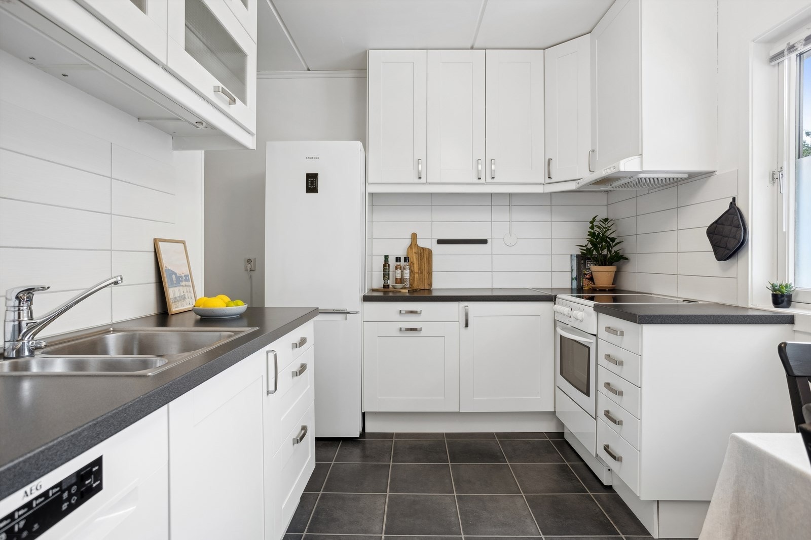 Fint IKEA kjøkken med laminert benkeplate. Profilerte hvite fronter. Flislagt over benkeplater. Ventilator med mekanisk avtrekk. Galleribilde
