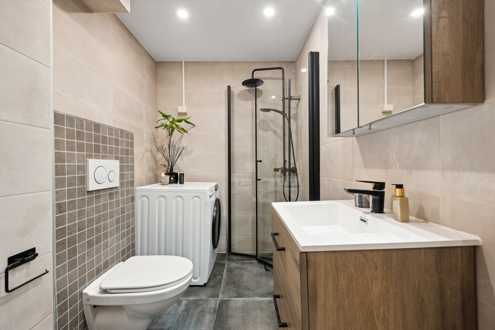 Badet er utstyrt med svingbare dusjvegger av glass, vegghengt toalett med skjult sisterne, servant med skuffer og ettreps kran og speilskap med lysarmatur. Galleribilde