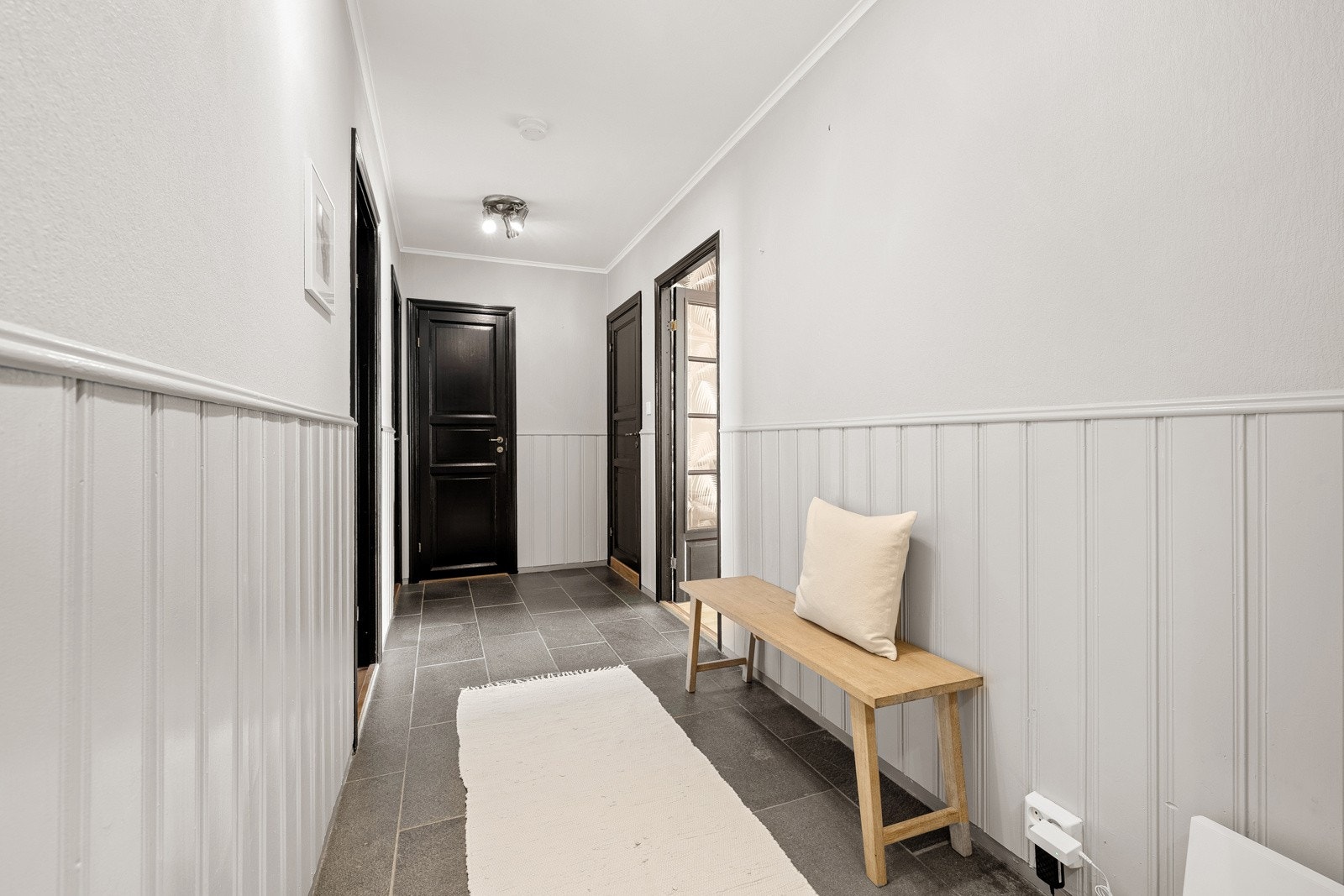 Rommet gir et lunt førsteinntrykk med skiferfliser på gulvet og en kombinasjon av panel og tapet på veggene. Galleribilde