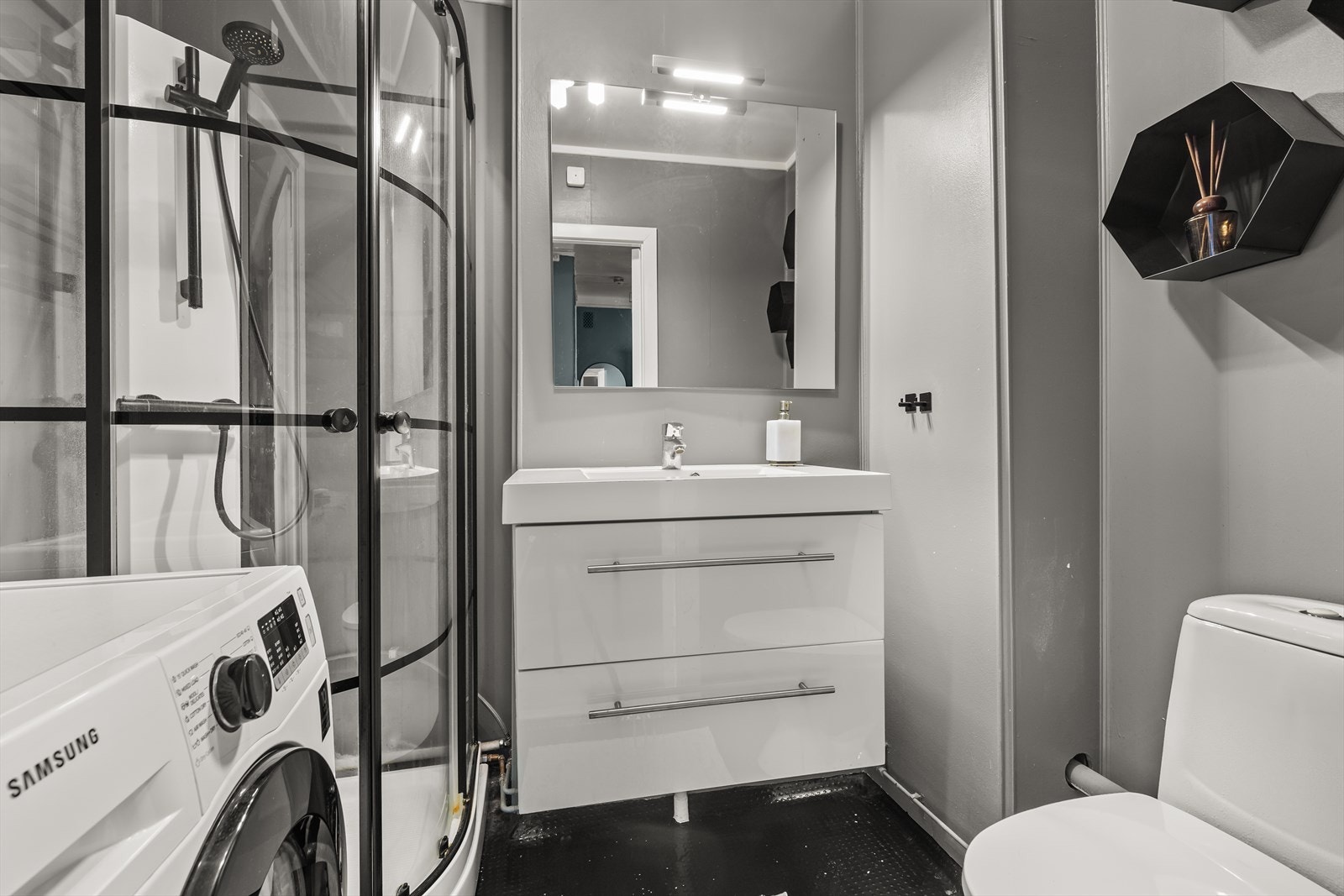 Eldre baderom med dusjkabinett, servantskap med speil, wc, opplegg for vaskemaskin og tørketrommel. Galleribilde