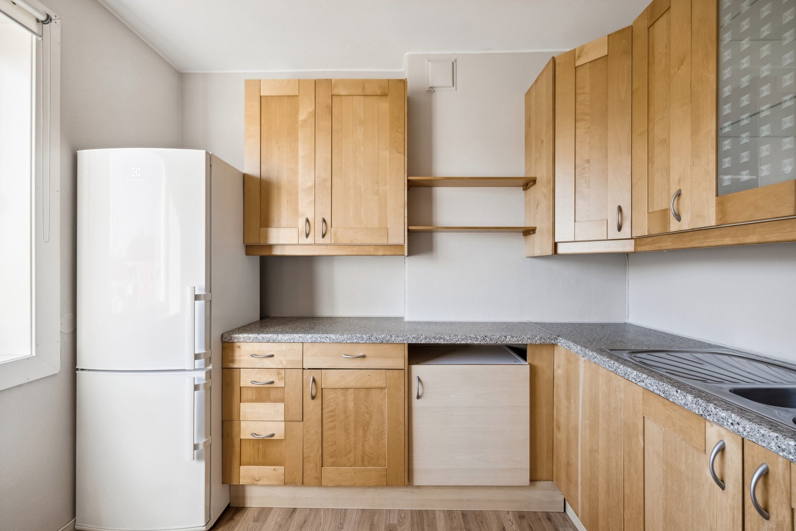 Kjøkkeninnredning med glatte finerte skapfronter, laminert benkeplate, 1 1/2 oppvaskkum med benkebeslag, kjøkkenventilator med kullfiltet og frittstående hvitevarer som komfyr og kjøl/- fryseskap. Galleribilde