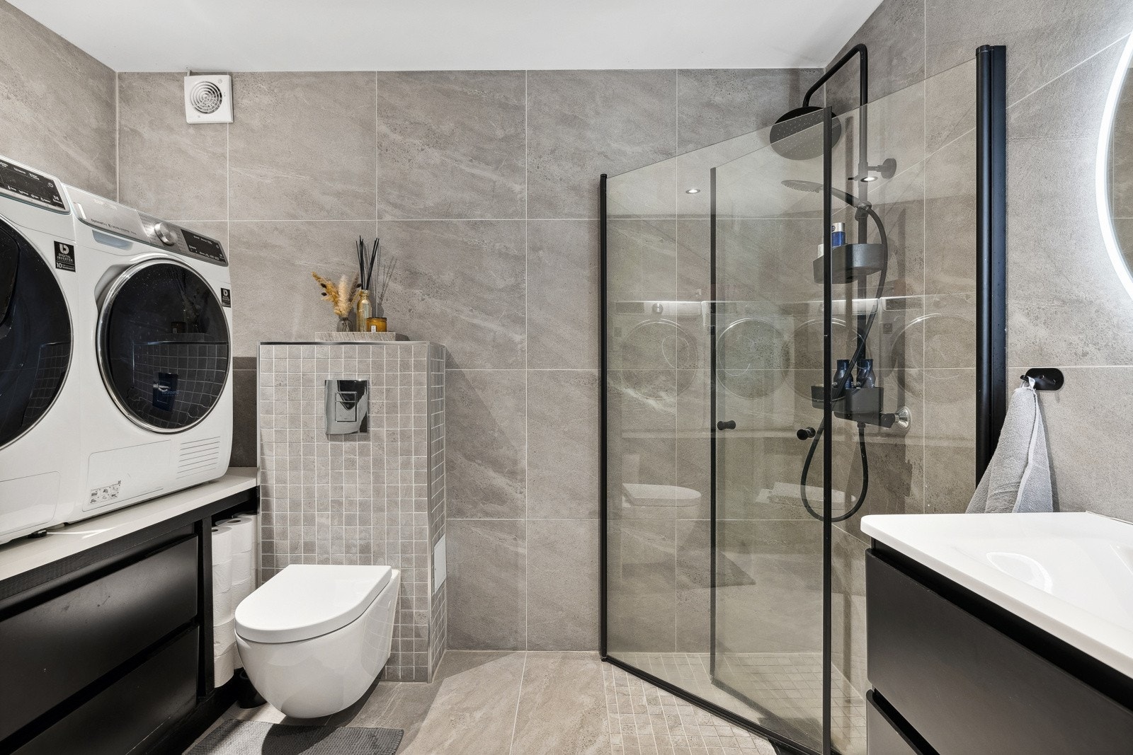 Baderommet har opplegg for vaskemaskin og tørketrommel i praktisk arbeidshøyde på benk med skuffer for oppbevaring. Galleribilde