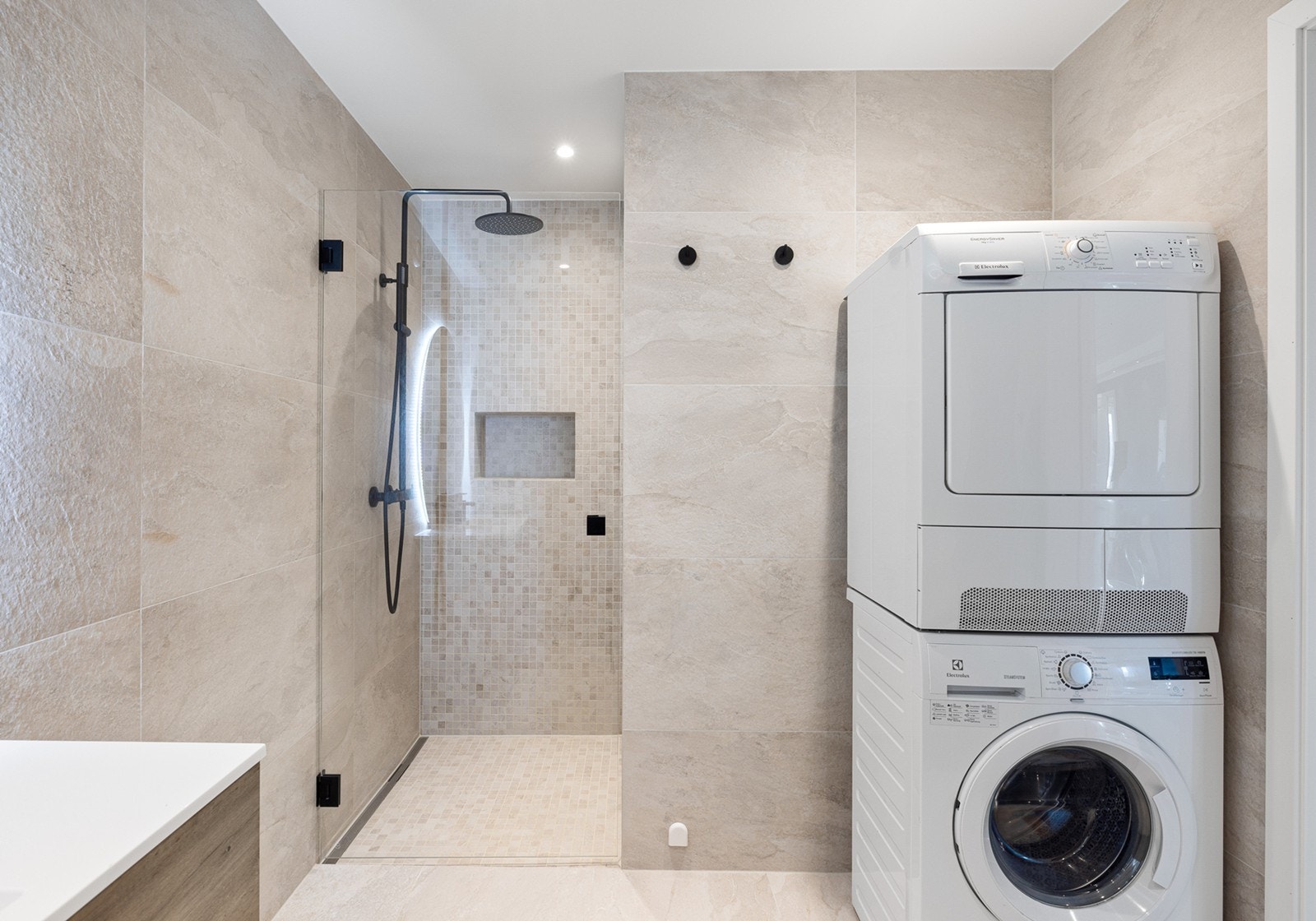 Boligen har et lekkert baderom med store, beige fliser på gulv og vegger, underliggende gulvvarme og downlights i himling. Badet ble pusset opp i 2024 og har moderne utforming. Galleribilde