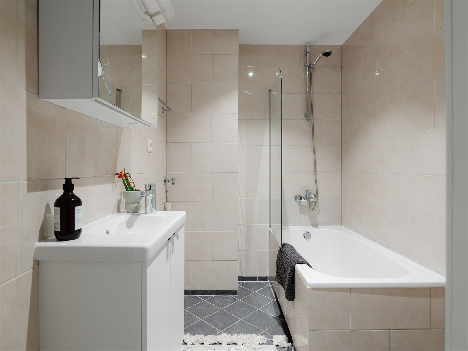 Badet er tidløst, med lyse fliser på vegger og mørke på gulv. Det er både opplegg for og plass til vaskemaskin i hjørnet. Galleribilde