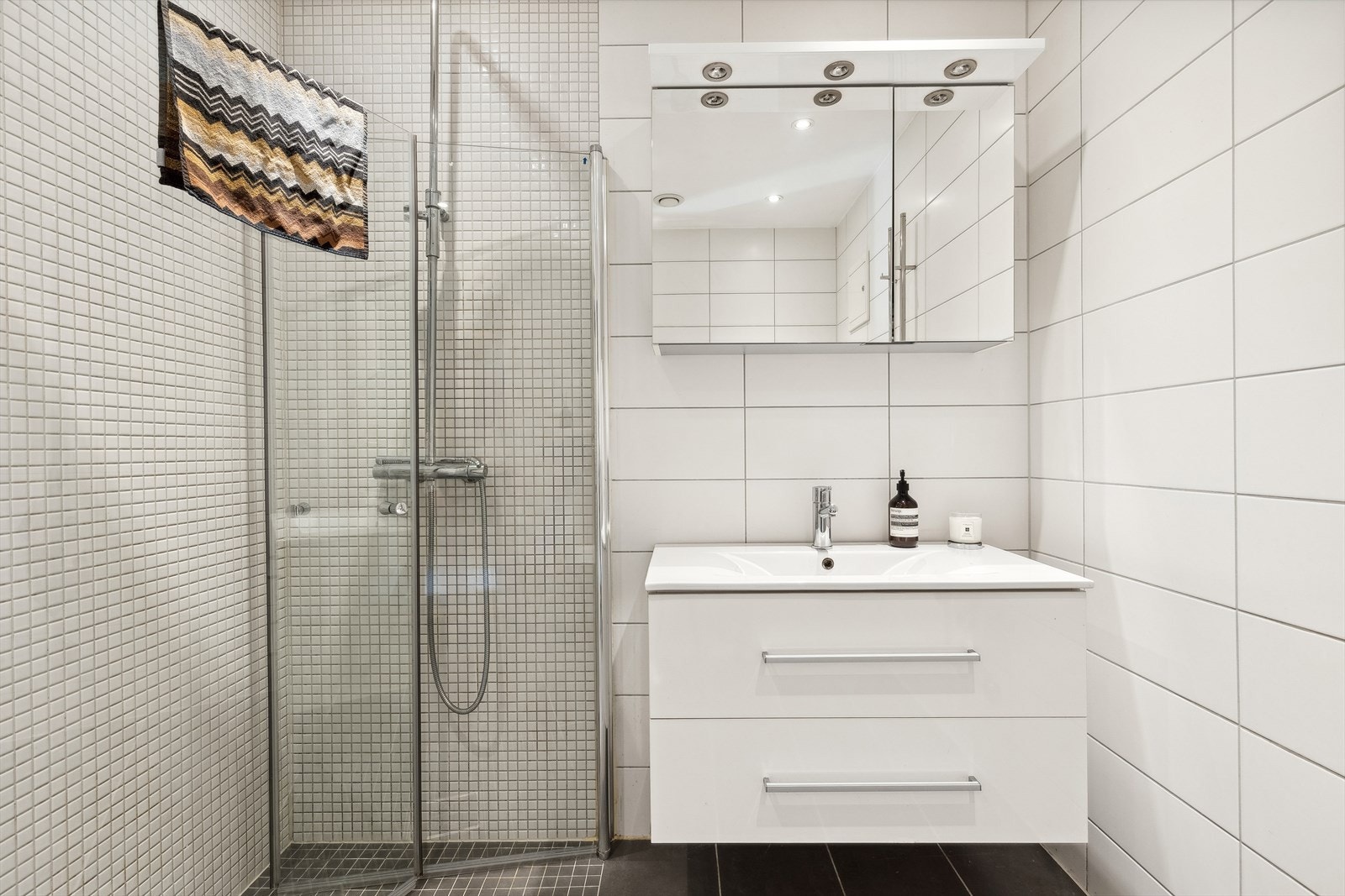 Badet er innredet med heldekkende servant på underskap med høyglansfolierte fronter, speilskap og veggmontert klosett Galleribilde