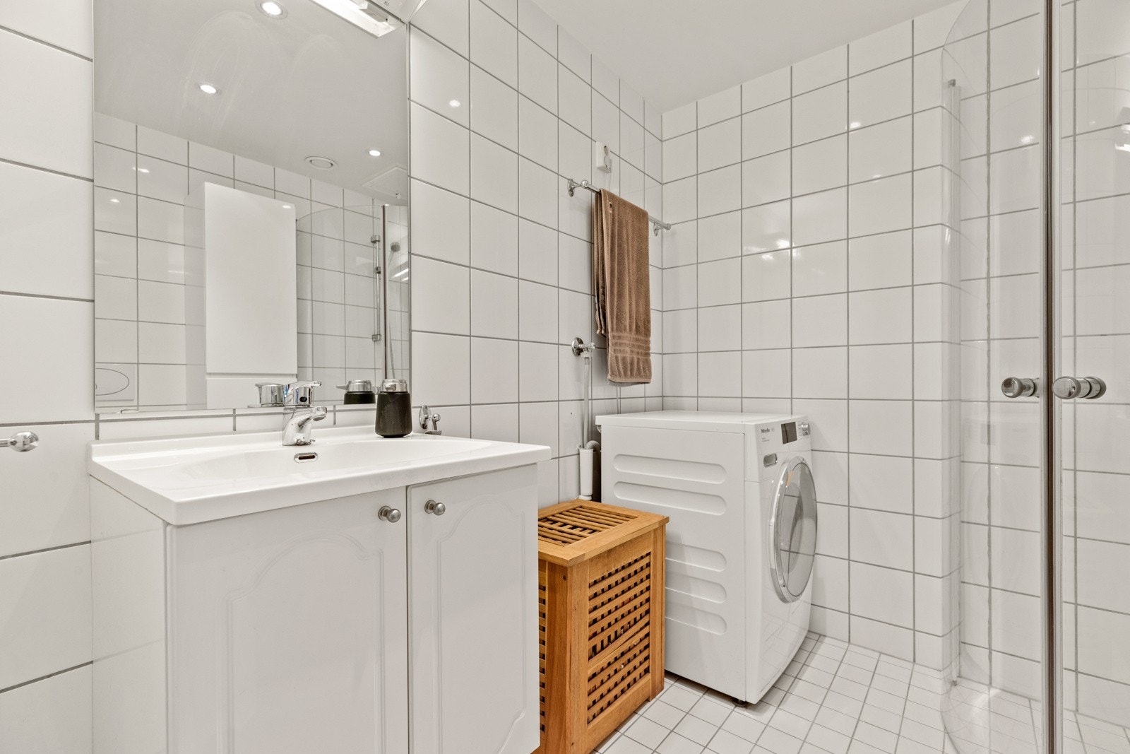 Badet er utstyrt med dusjhjørne med dører i glass, servantinnredning med underskap, høyskap og vegghengt toalett. Det er opplegg for vaskemaskin. Galleribilde