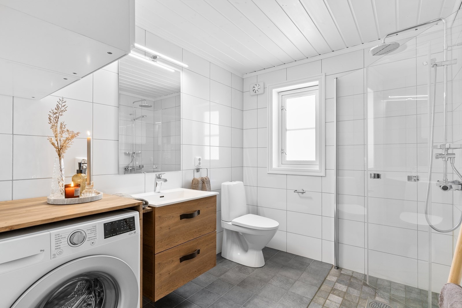 Bad har innredning med nedfelt servant, toalett, dusjvegger/hjørne og opplegg for vaskemaskin. Veggene har fliser, taket har panel og gulvet er flislagt med elektriskevarmekabler. Galleribilde