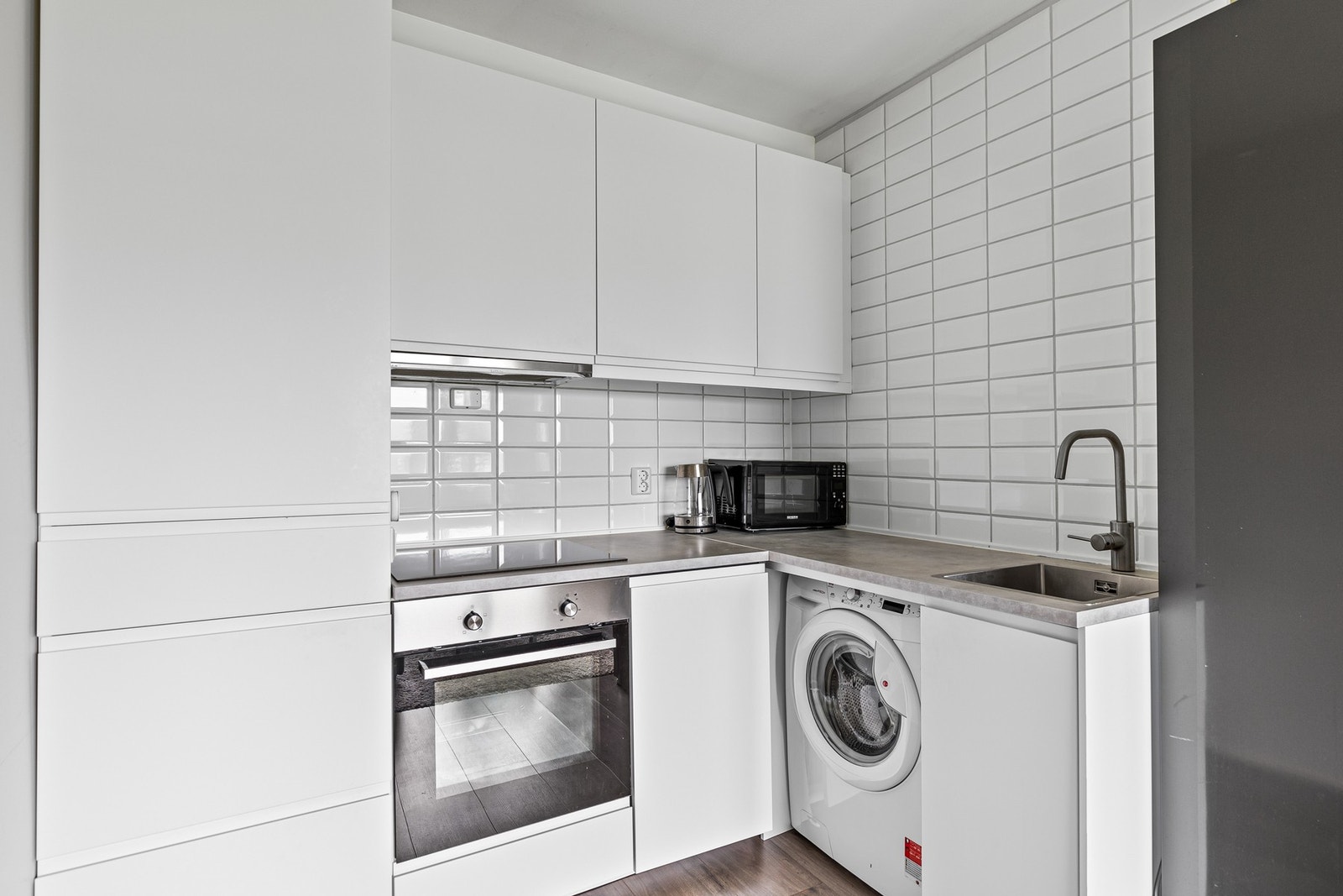 Moderne kjøkken med kjøleskap, oppvaskmaskin, platetopp og stekeovn som integrerte hvitevarer. Galleribilde