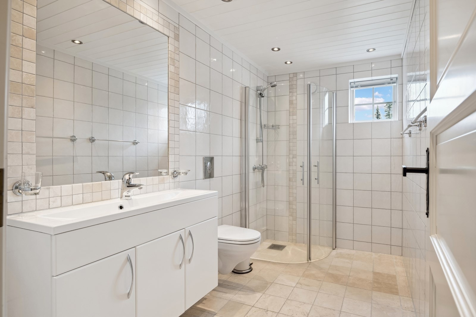 Lyst bad flislagt med hvite og sand/beige fliser som gir badet en lun atmosfære. Galleribilde