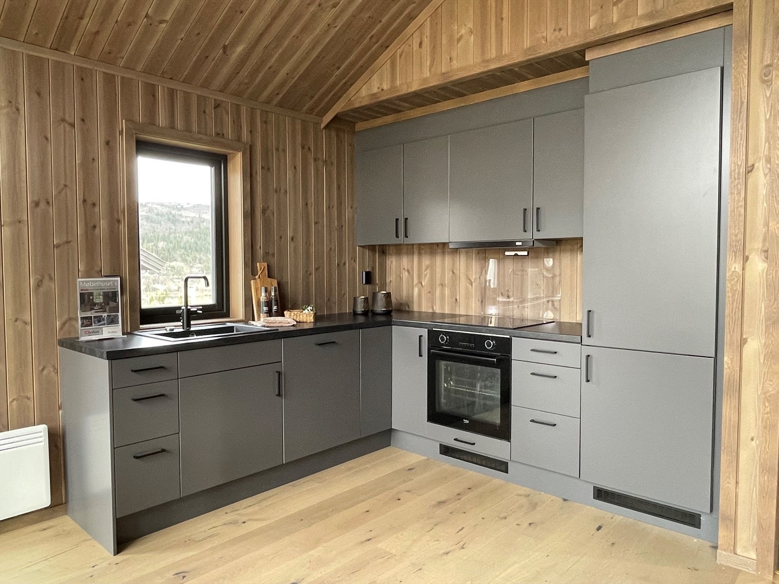 Kjøkkeninnredningen er stilfull med mørke, glatte fronter og sorte detaljer. Integrerte hvitevarer som stekeovn, koketopp og ventilator i sort utførelse. Galleribilde