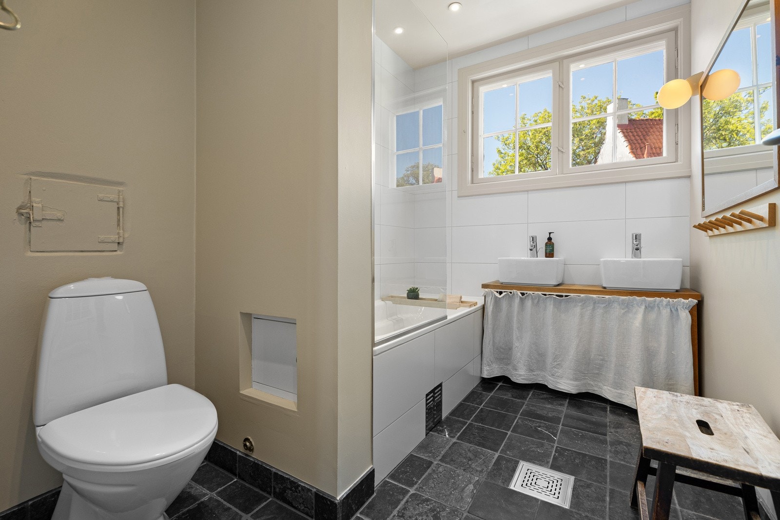 Inneholder servantbolle på heltre benkeplate, speil med lysarmatur på vegg, toalett og innebygd badekar Galleribilde