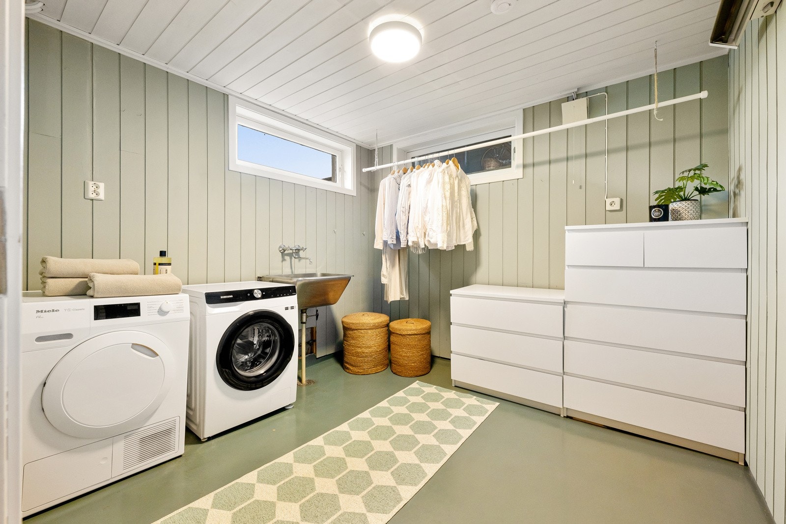 Vaskerommet er også plassert i kjelleren. Veggene er kledd med panel, malt i en dus, moderne grønnfarge som matcher gulvet. Galleribilde