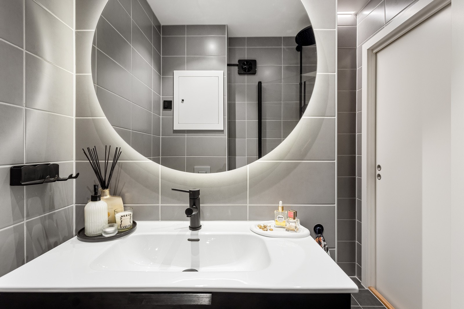 Moderne baderomsinnredning med skuffer og heldekkende servant, rundt speil med integrert belysning over. Galleribilde