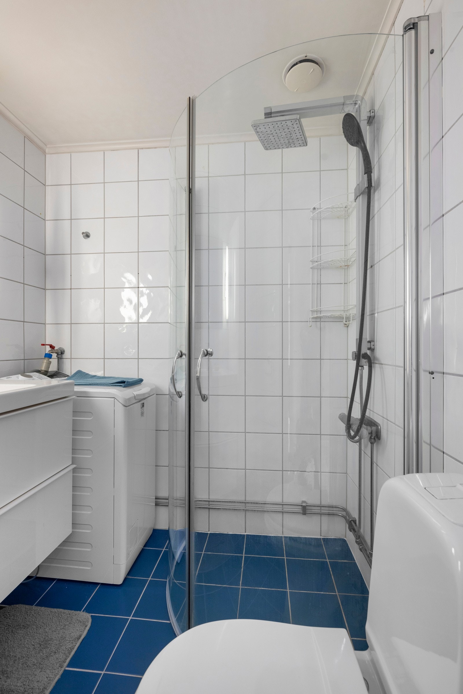 Badet er utstyrt med toalett, opplegg for vaskemaskin, samt et dusjhjørne med buede, innfellbare glassdører, regnfallsdusj og håndgarnityr Galleribilde
