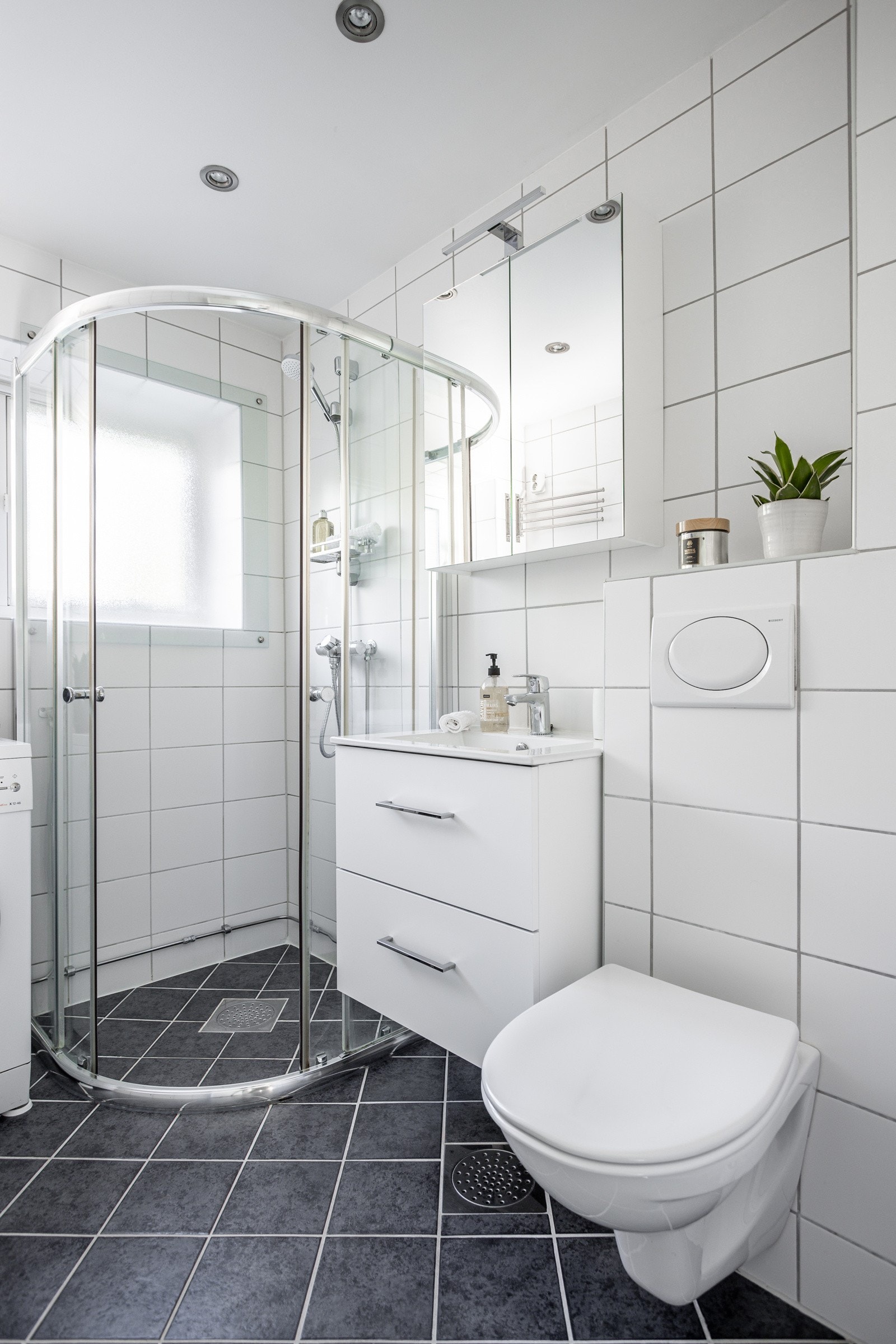 Baderommet har mørke fliser på gulv med gulvvarme, lyse fliser på veggene og downlights i himlingen. Galleribilde