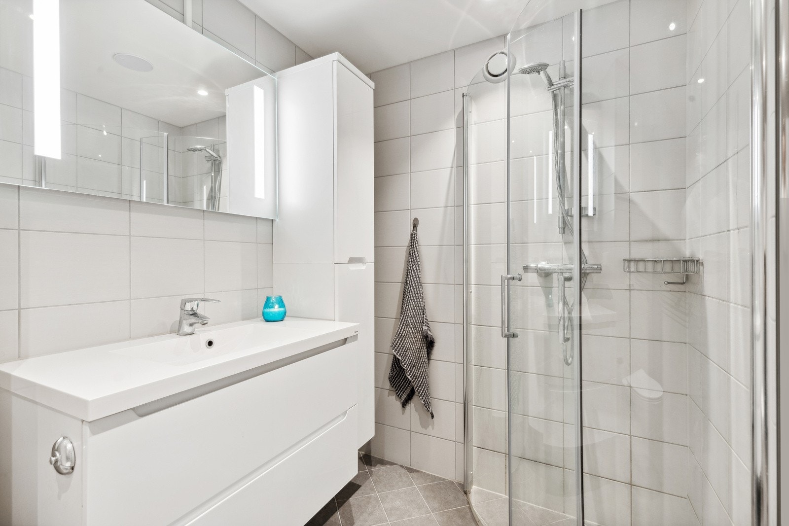 Badet inneholder vegghengt servantskap med ett-greps armatur, vVegghengt speil med belysning og stikkontakt på vegg, dusjhjørne med innfellbare glassdører og to-greps armatur påkoblet hånddusj og vegghengt toalett. Mekanisk avtrekksventil på vegg. Galleribilde
