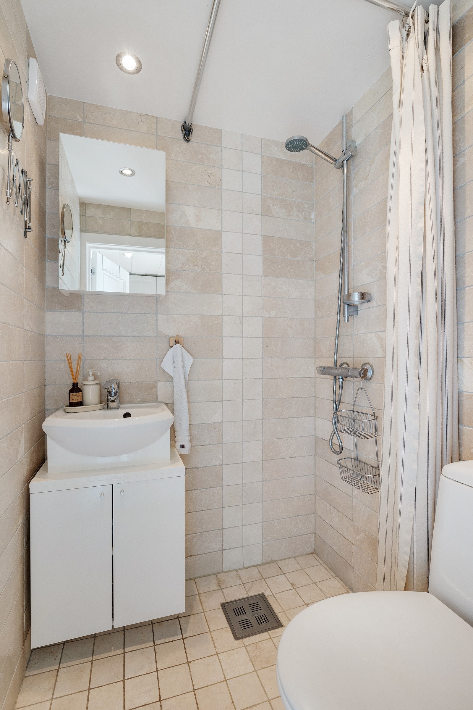 Videre inneholder badet dusjhjørne med to-greps armatur påkoblet hånddusj, dusjforheng, samt gulvstående toalett. Galleribilde