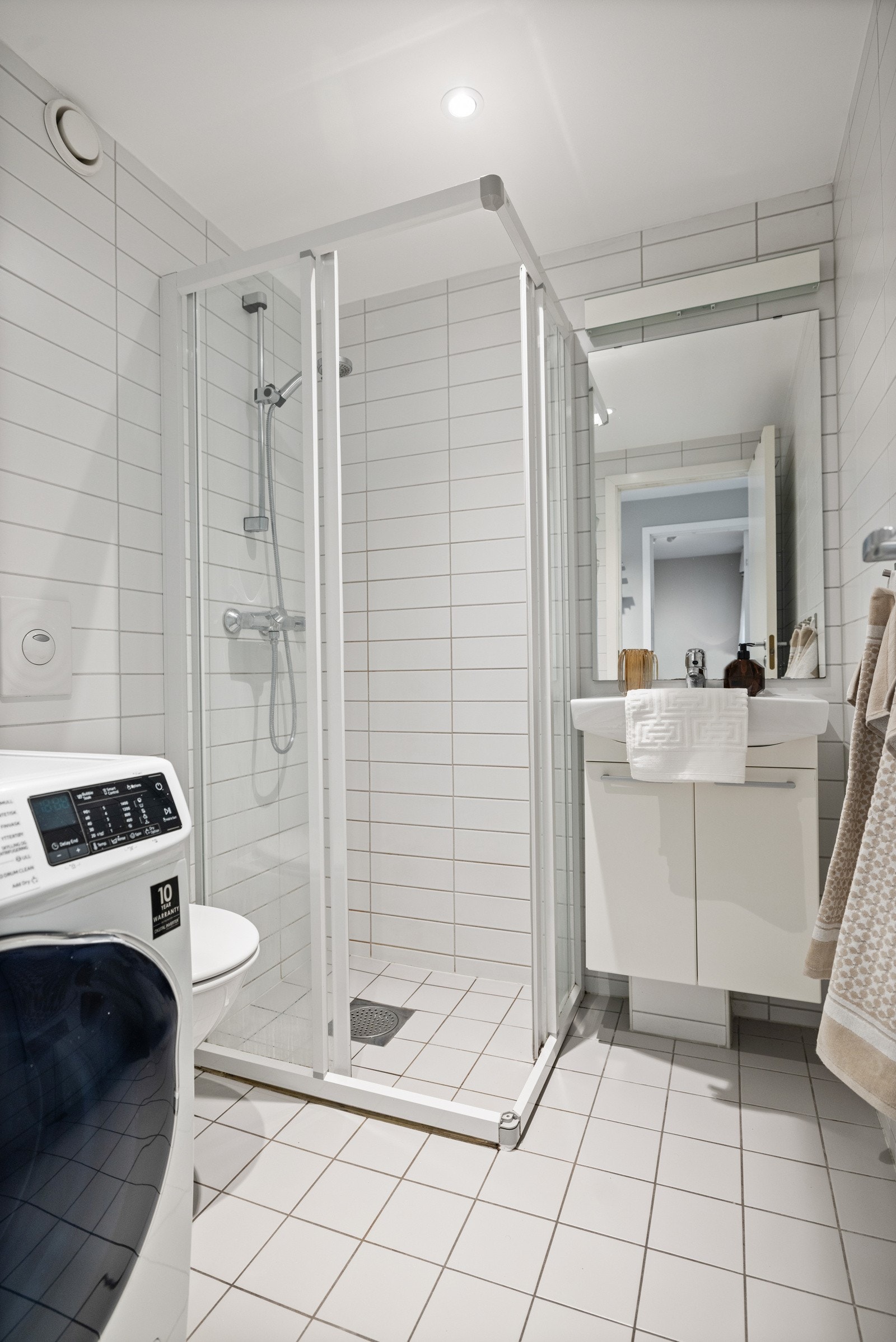Badet er utstyrt med vegghengt skap med speil, dusjhjørne og klosett montert på vegg med sisterne. Galleribilde