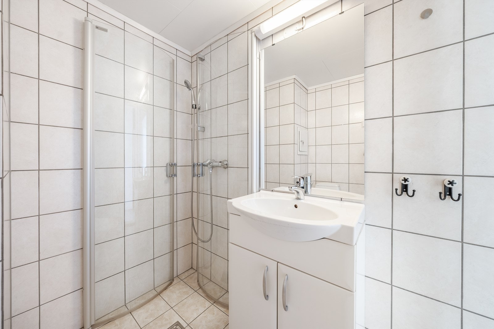 Fra entreen er det adkomst til boligens bad. Her er det flislagt bad med gulvvarme, og opplegg til vaskemaskin. Videre er det toalett, åpen dusjløsning med dusjdører og servantinnredning med underskap og speil. Galleribilde