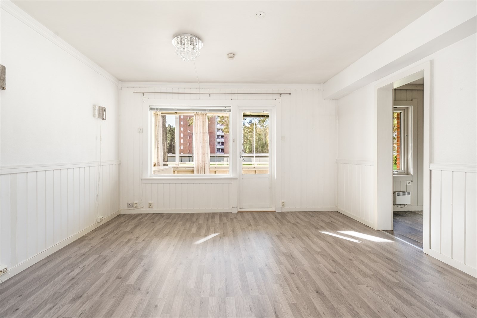 Lys stue med plass til sofa og spisebord. Her er det gode vindusflater som slipper inn rikelig med naturlig lys. Det er laminat på gulv, malt brystpanel på vegger og malt tak. Galleribilde