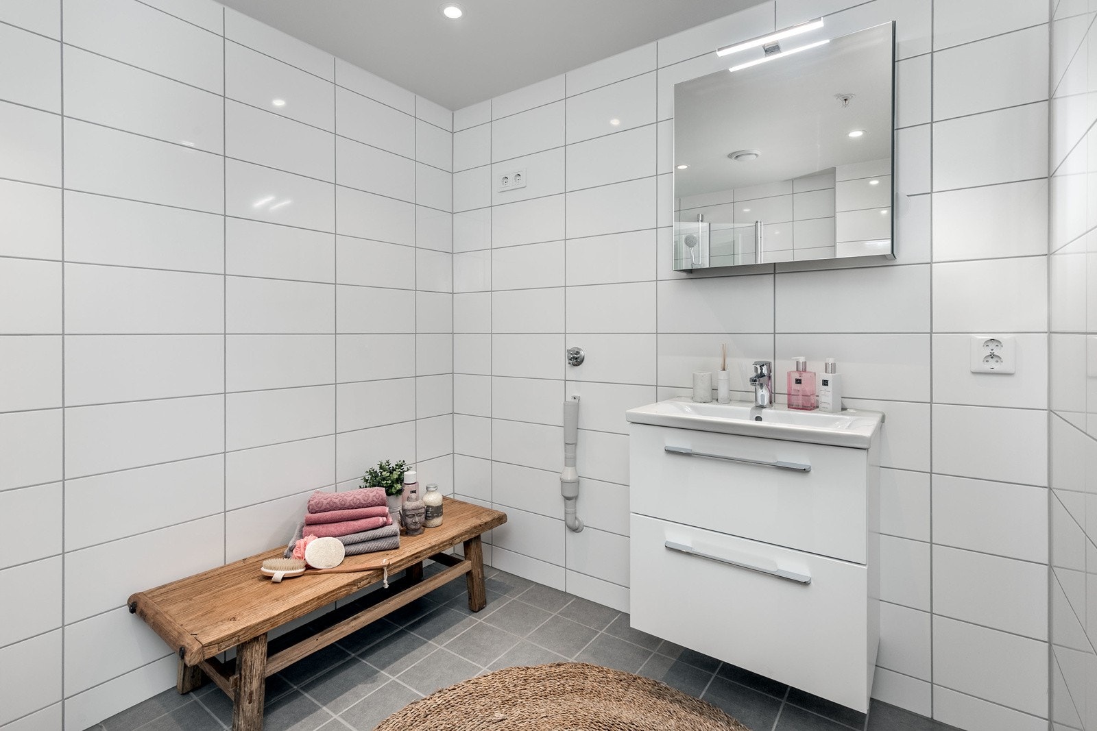 Delikat og smakfullt bad med flislagte overflater og varmekabler i gulv. Innredningen består av moderne skuffeinnredning med servant og speil over servant m/toppmontert belysning. Videre er det vegghengt toalett i hvitt porselen med dempesete. Galleribilde