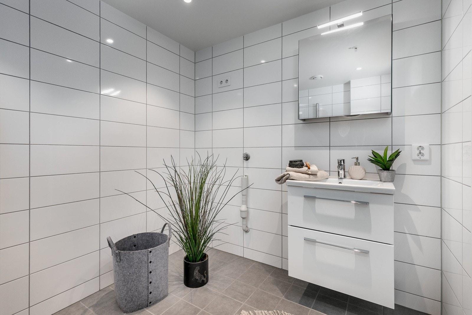 Delikat og smakfullt bad med flislagte overflater og varmekabler i gulv. Innredningen består av moderne skuffeinnredning med servant og speil over servant m/toppmontert belysning. Videre er det vegghengt toalett i hvitt porselen med dempesete. Galleribilde