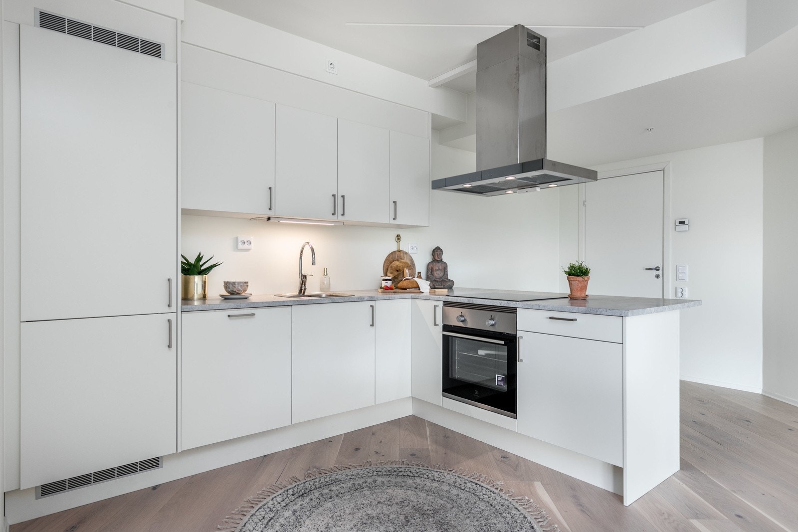 Innredning med hvite slette fronter med foring opp til tak. Laminert benkeplate i lys betong utførelse med nedfelt oppvaskkum i rustfritt stål. Galleribilde