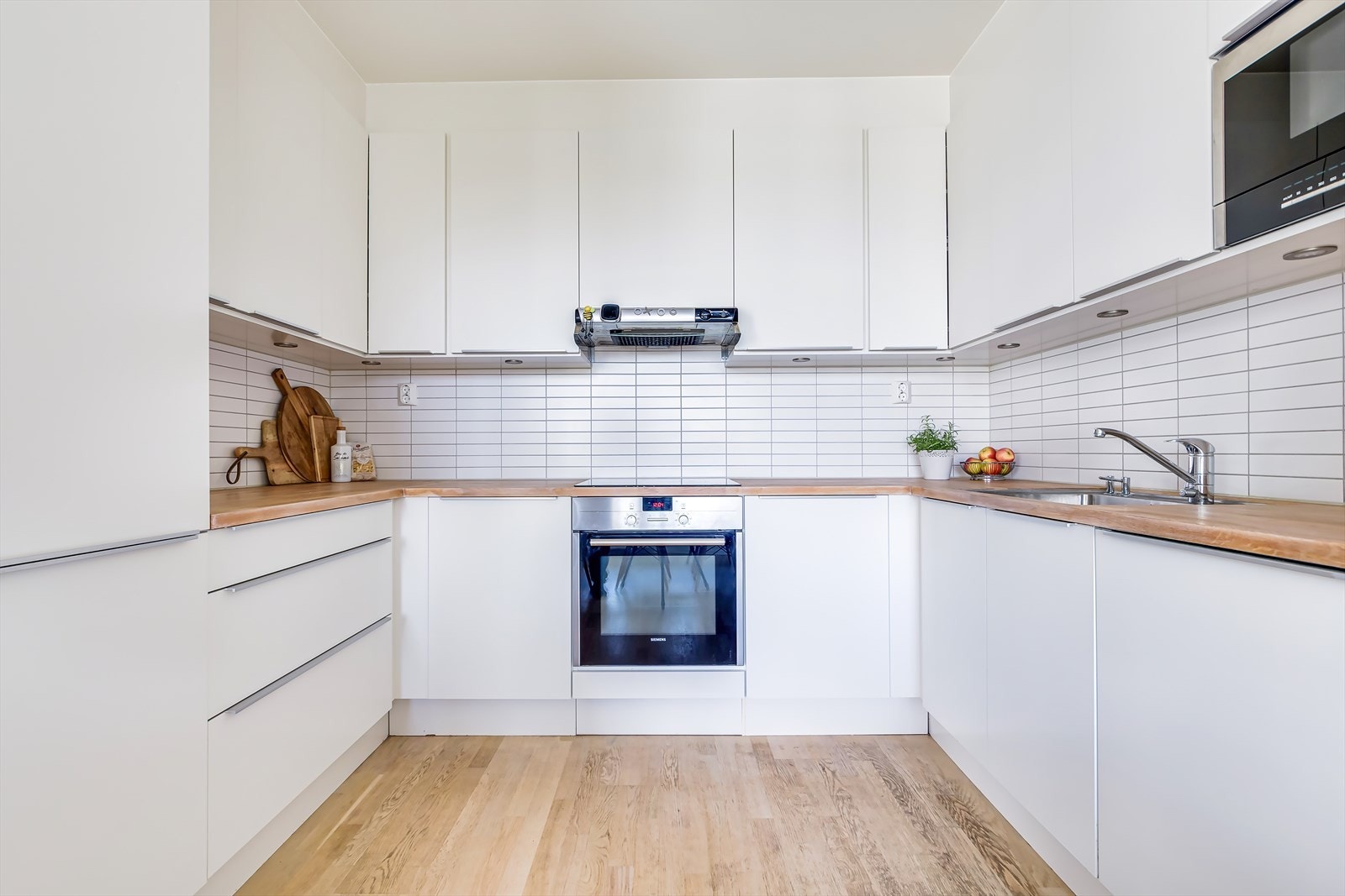 Stilrent HTH-kjøkken fra 2014 med hvite fronter, fliser på bakvegg og heltre benkeplate Galleribilde