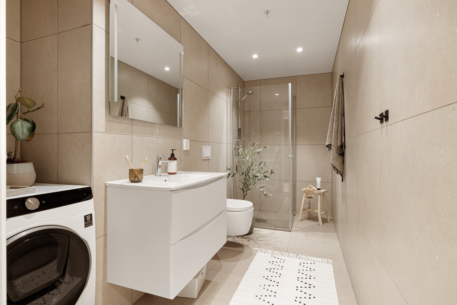 Badet er utstyrt med 60x60 fliser, spotter, dusjhjørnet, vegghengt toalett, innredning med vask og opplegg for vaskemaskin Galleribilde