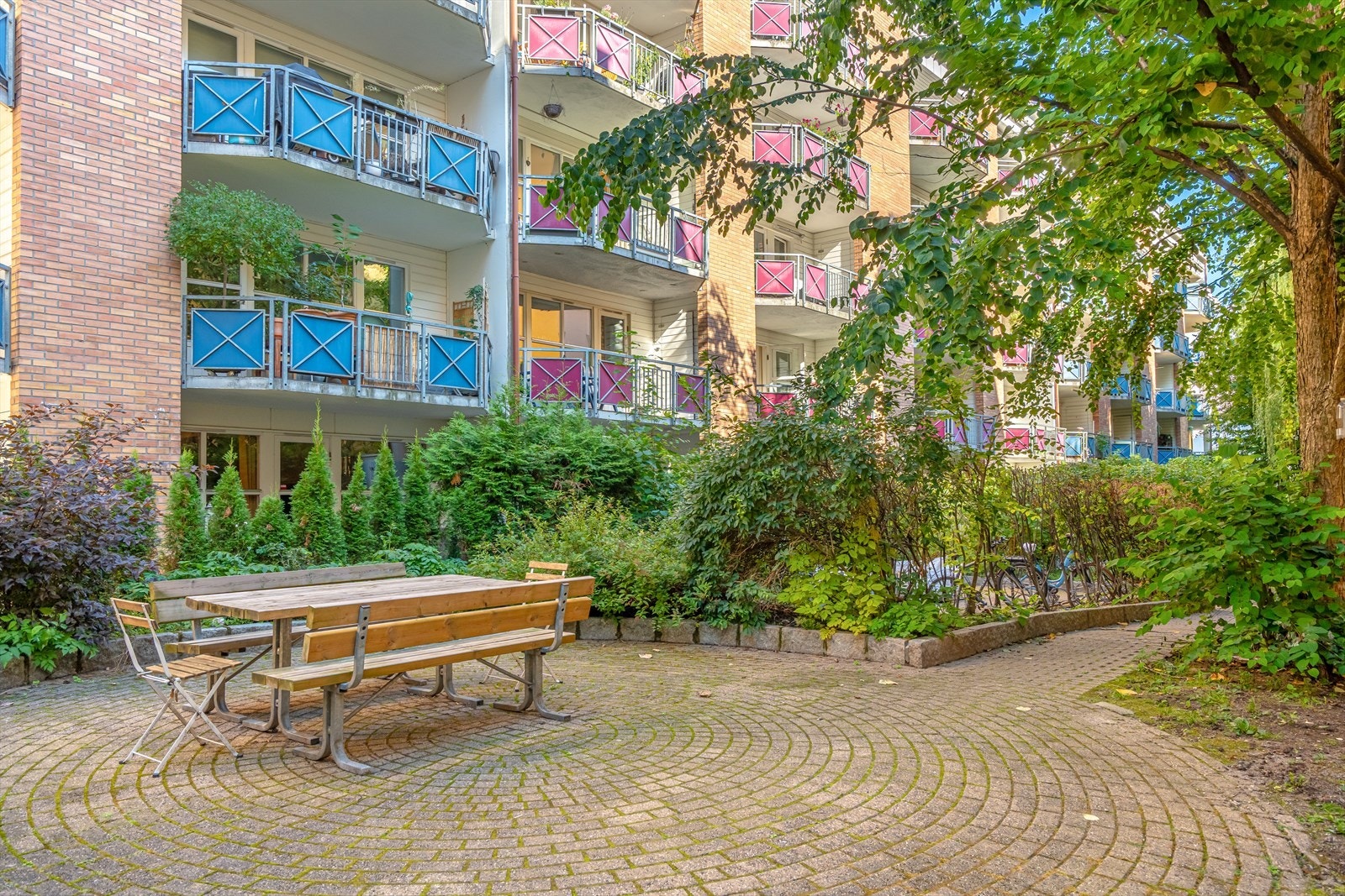I bakgården er det flere sittegrupper og sykkelparkering. Pent opparbeidet tomt med brostein og beplantning Galleribilde