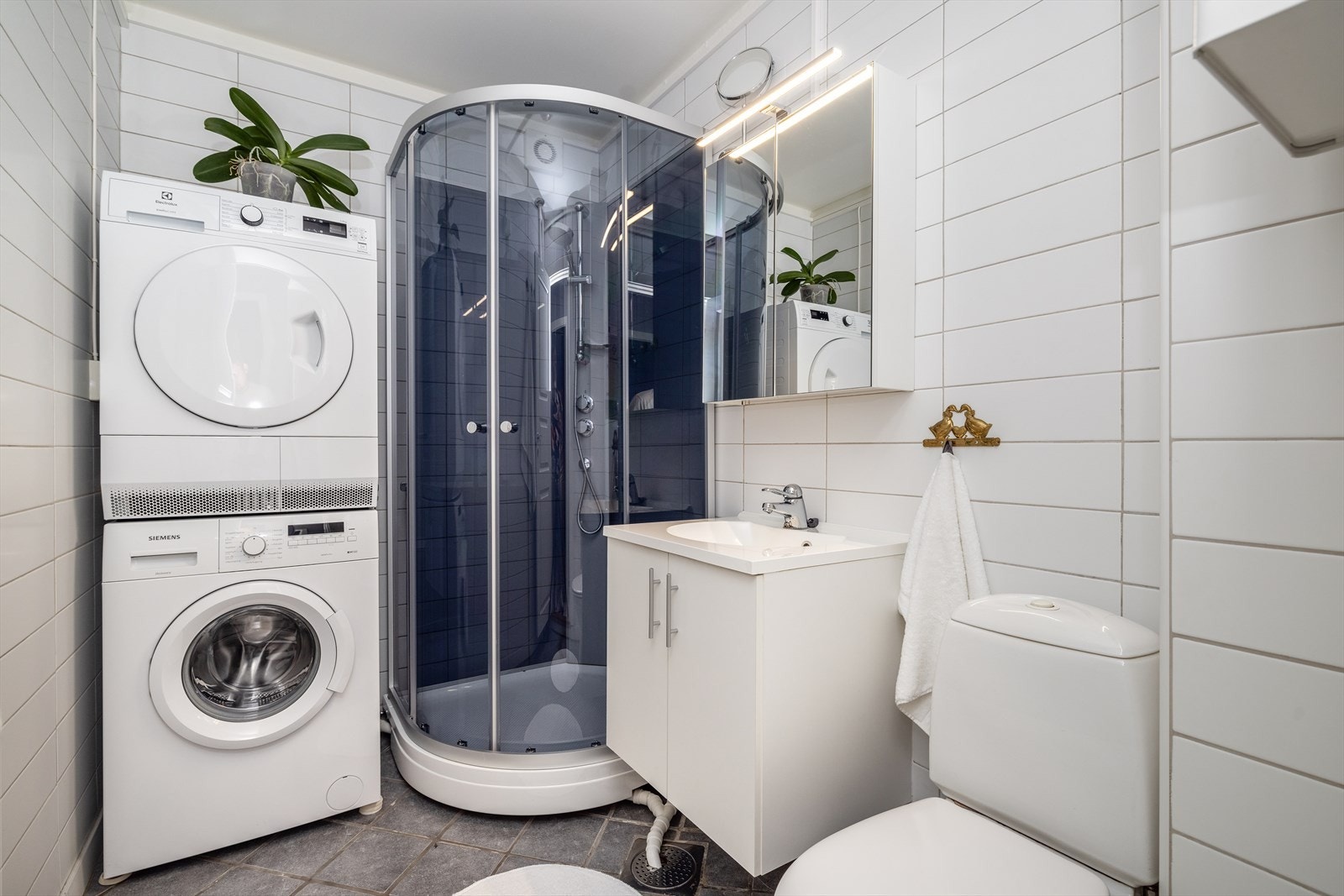 Bad fra 2010 med flis på gulv og vegger. Her er det dusjkabinett, toalett og innredning med heldekkende hvit vask, underskap med slette fronter, overskap med speildører og lys. Badet har også opplegg for vaskemaskin og tørketrommel. Varmekabler i gulv. Galleribilde
