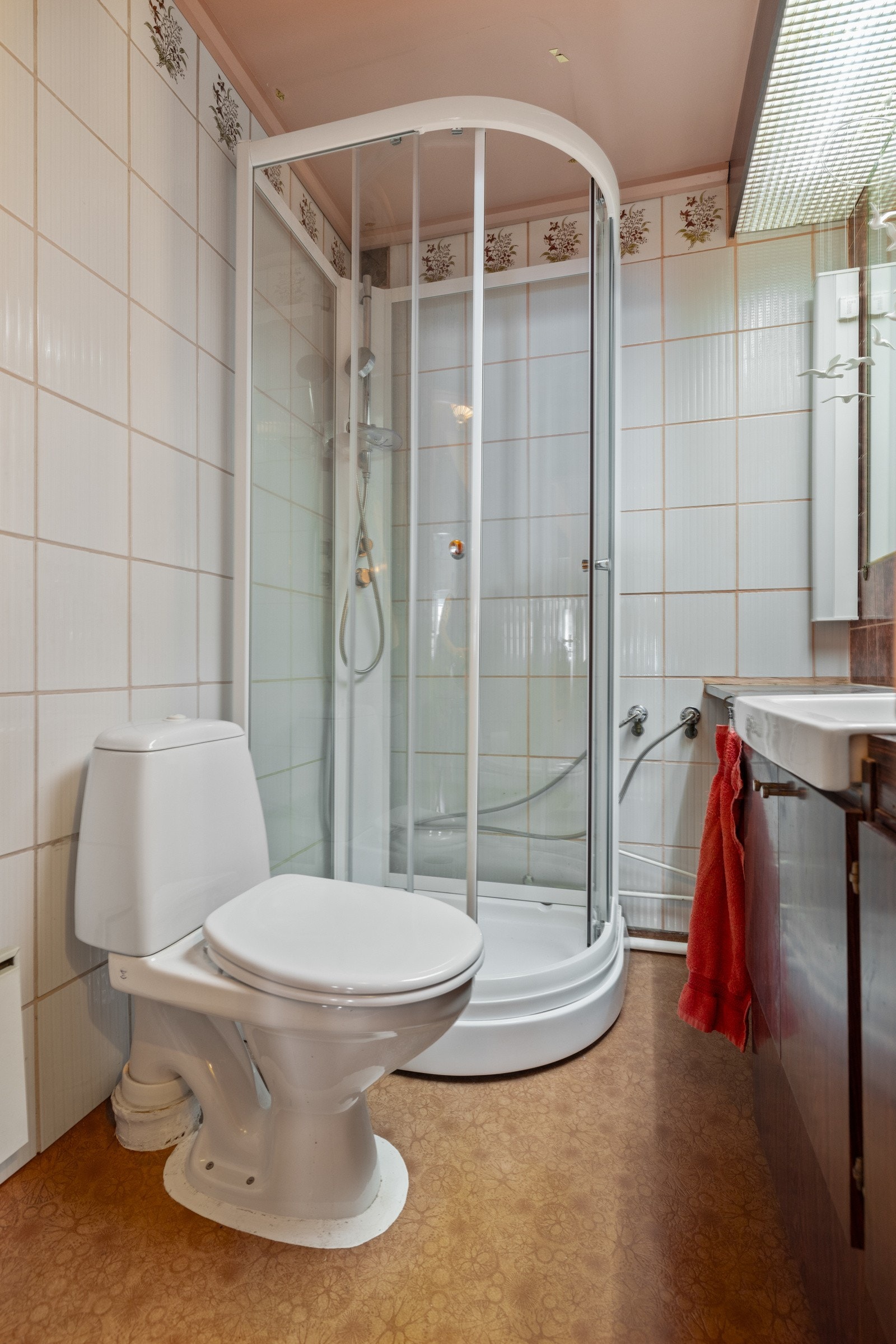 Badet har gulvbelegg, flislagte vegger og oppvarming med panelovn, samt et praktisk dusjkabinett montert i hjørnet Galleribilde