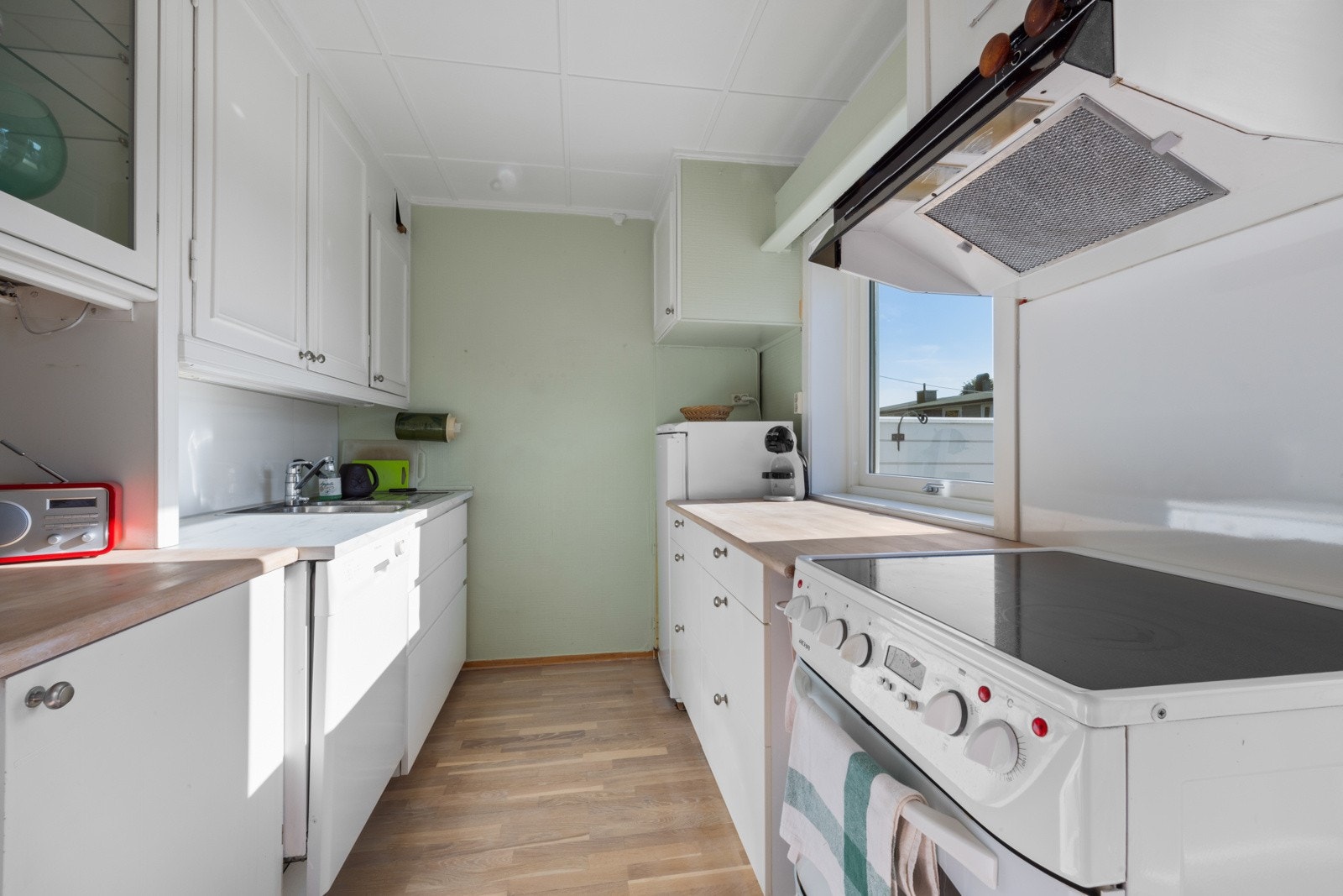 Kjøkkenet har en eldre innredning med hvite fronter, kombinert med benkeplater av hvit laminat og heltre Galleribilde