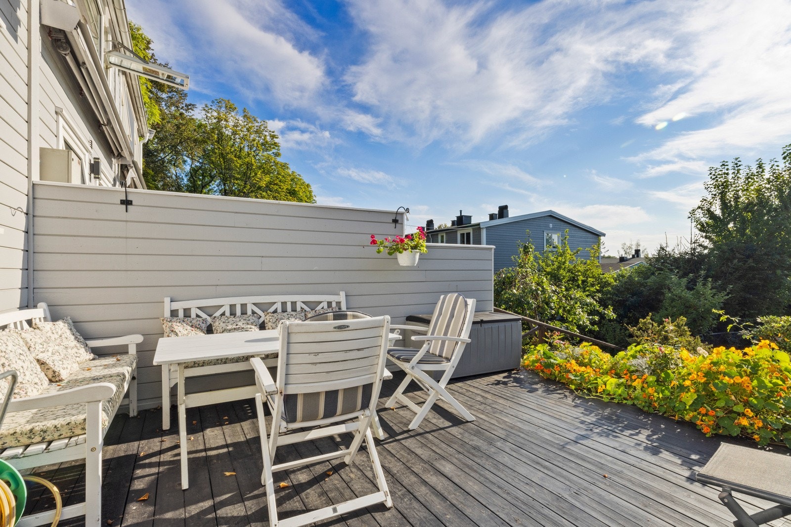 Det hyggelige uterommet er pent anlagt med dekke av terrassebord, skjermende levegger på siden, trapp ned til felleshagen og bugnende blomsterbed langs kanten mot hagen Galleribilde