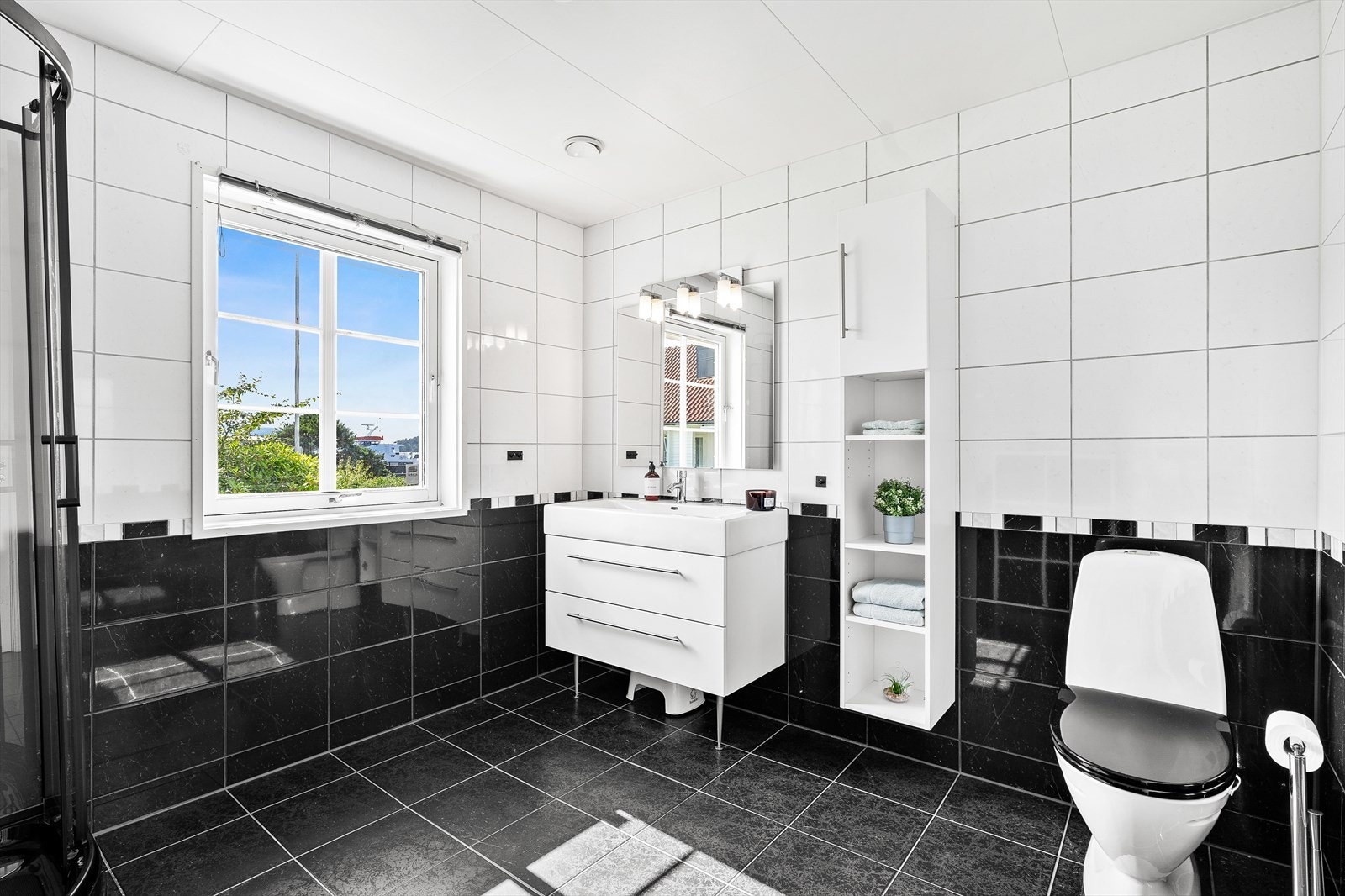 Badet er romslig og tidløst utført med lyse fliser på vegg mot mørke fliser på gulv. Galleribilde