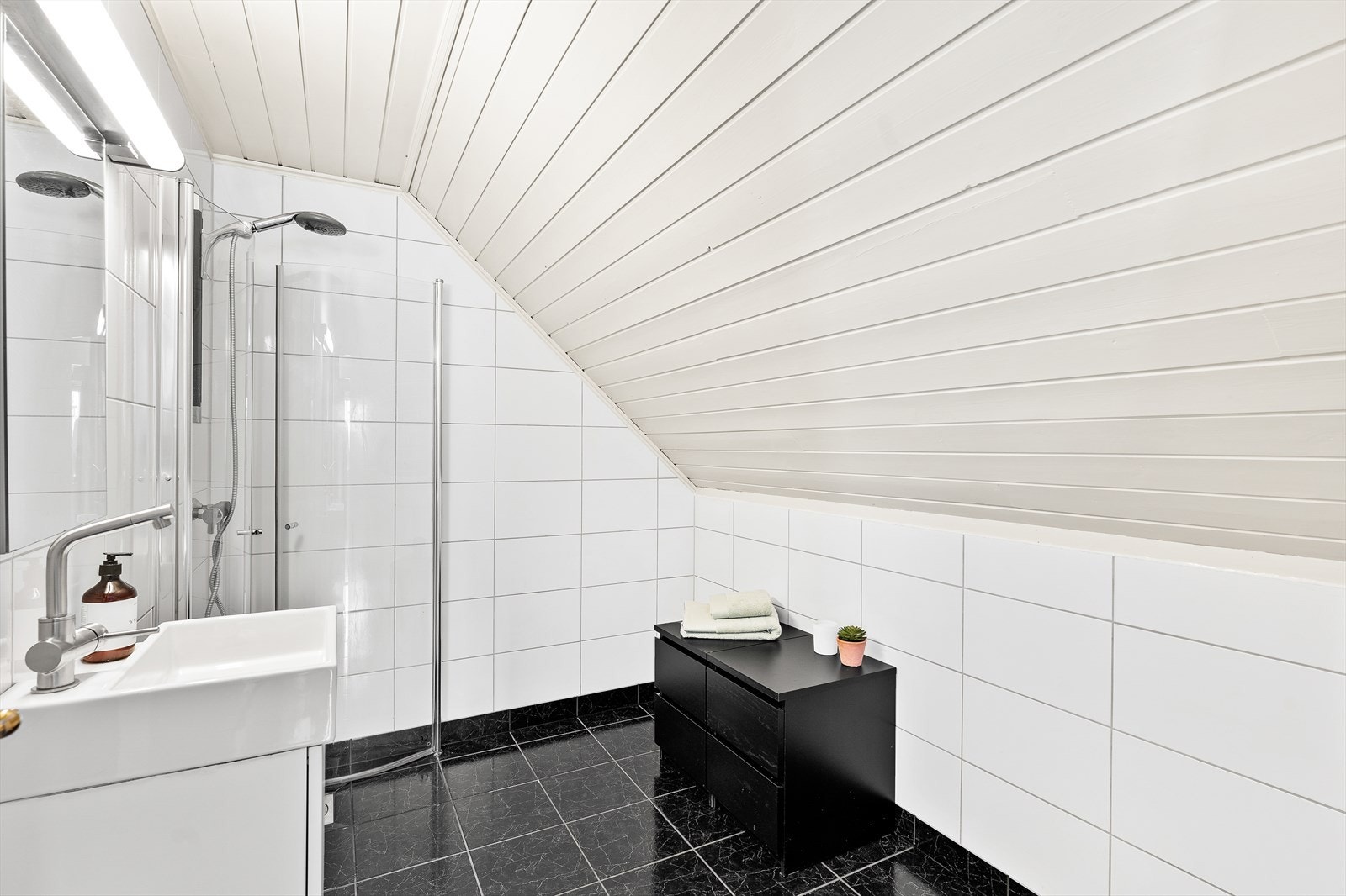 Badet er innredet med dusjhjørne med glassvegger, servant og toalett. Galleribilde