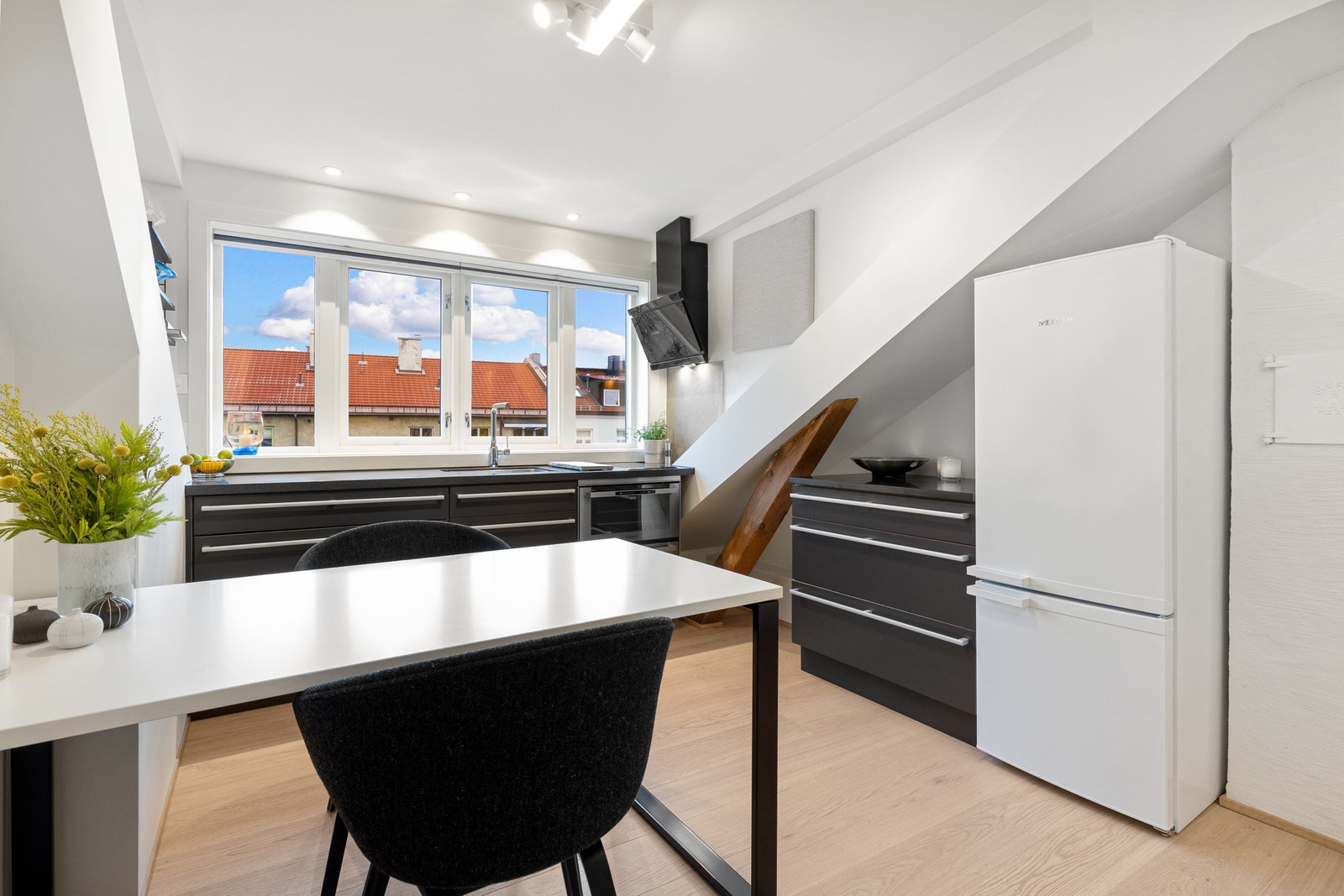 Romslig kjøkken der innredningen er fra Kvänum med corian benkeplate under vinduer og benkeplate i sten(larvikitt) mot kombikjøleskap. Galleribilde