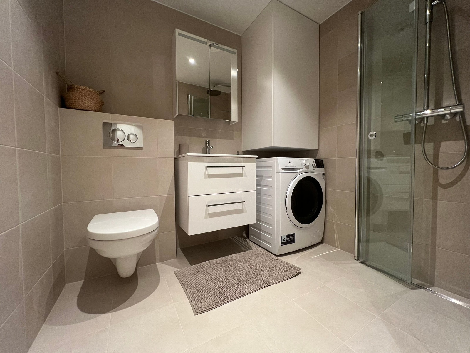 Bad med toalett, vask, speilskap, kombinert vaskemaskin/tørketrommel og dusj Galleribilde
