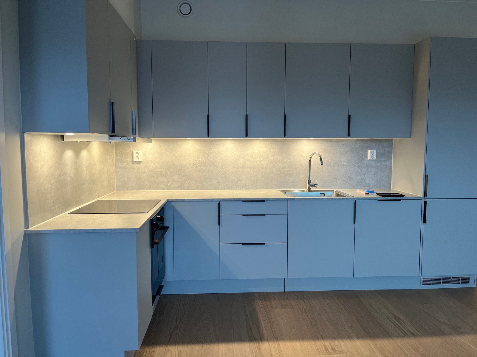 Lysgrått kjøkken med mange skap og downlights. Kjøl/frys, platetopp induksjon, stekeovn, opp vaskmaskin. Galleribilde