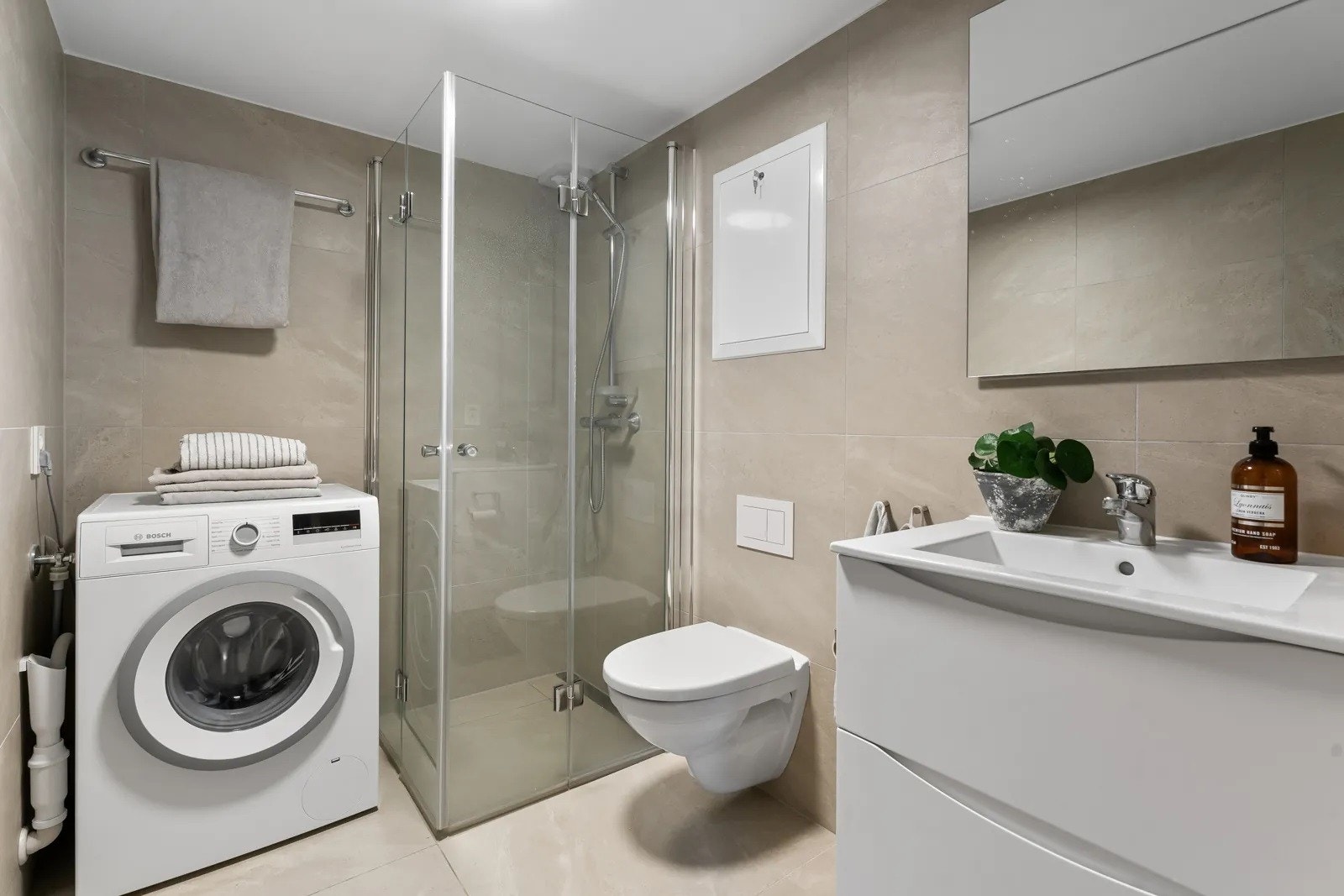 Badet i hybellleilighet har lyse storformatfliser på gulv og vegger, gulvvarme og vaskemaskin. Galleribilde