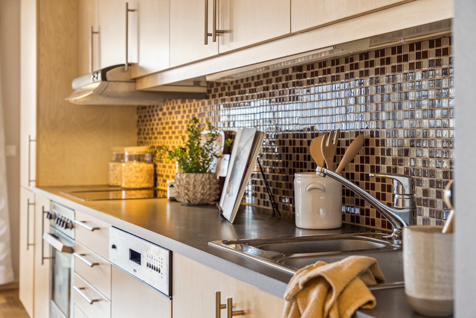 Benkelys og stikkontakter over kjøkkenbenken gir optimal arbeidsbelysning, mens fliser mellom benk og overskap tilfører et moderne uttrykk. Galleribilde