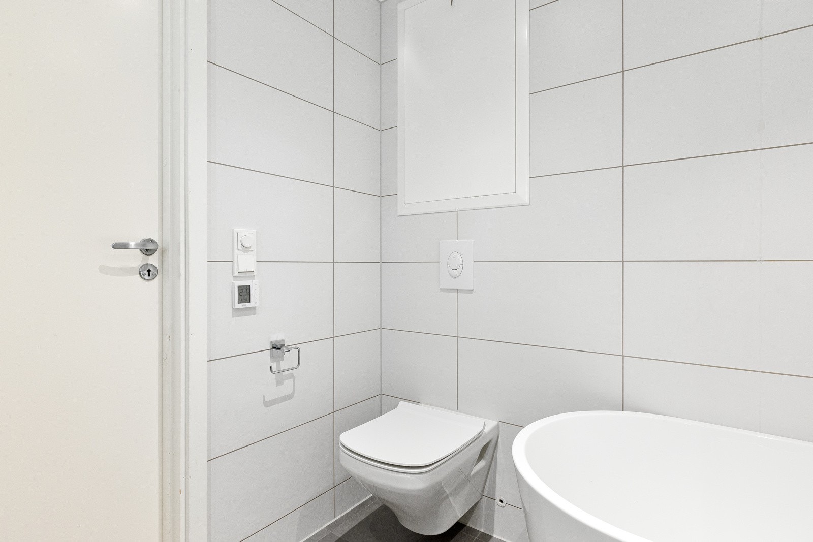 Innredningen inkluderer vegghengt toalett, servant med underskap, speil med integrert belysning og en dusjløsning i badekar med dører av herdet glass. Galleribilde