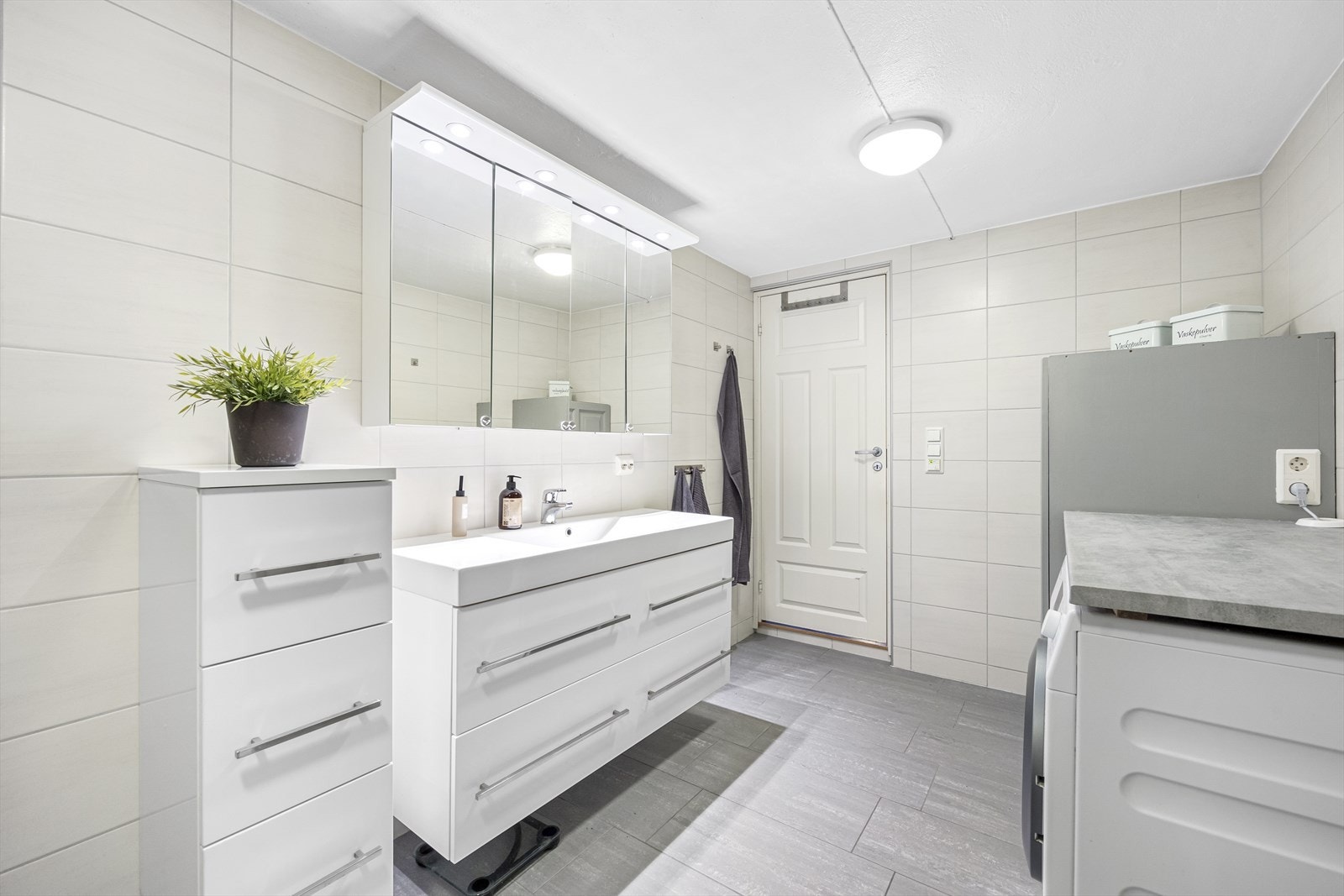 Bad/vaskerom i underetasje. Også dette badet ble pusset opp i 2011. Flislagt på gulv og vegger med varmekabler. Badet er innredet med innbokset varmtvannsbereder, opplgg til vaskemaskin og tørketrommel med praktisk benkeplate over. Baderomsinnredning. Galleribilde