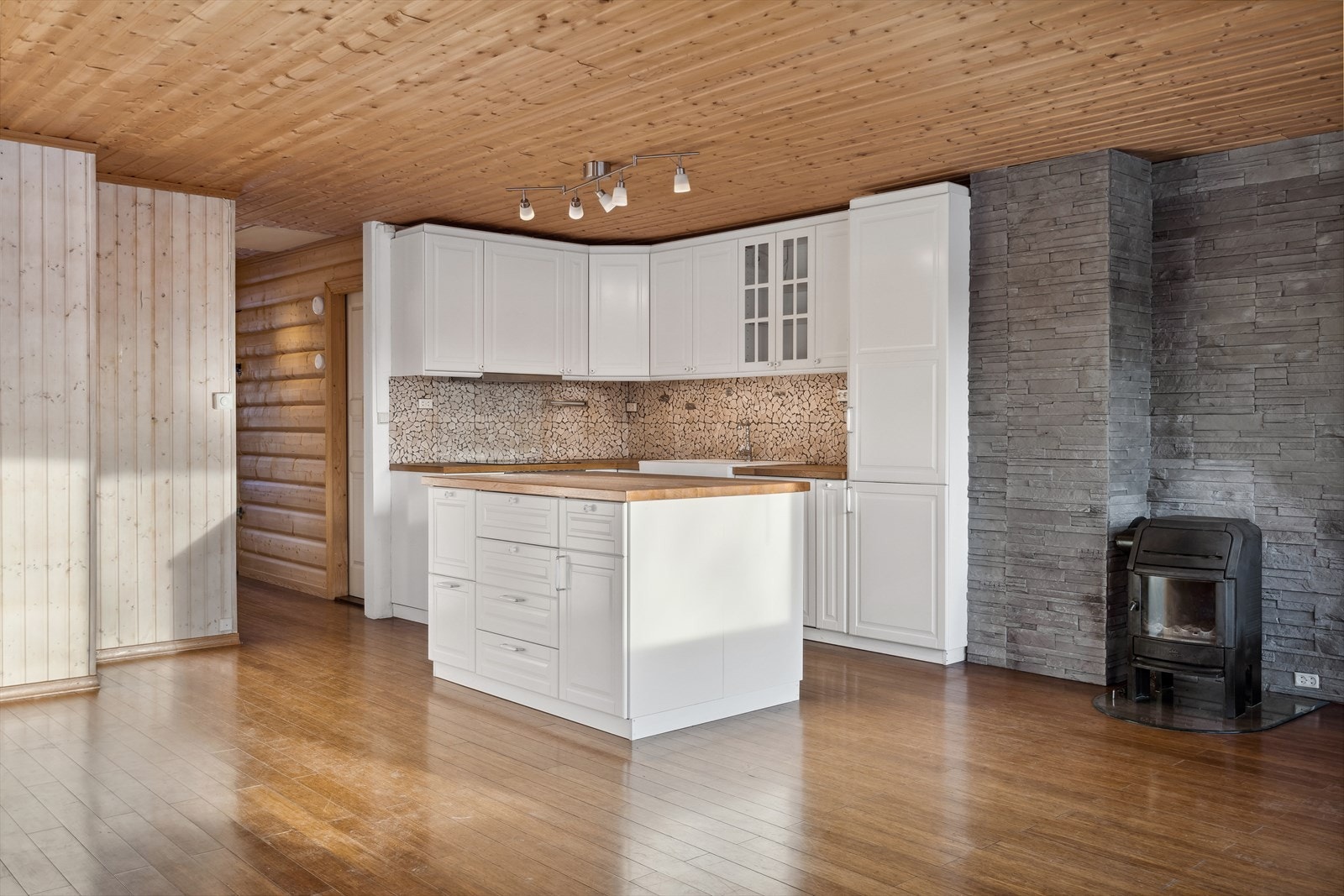 Gulv belagt med heltregulv, og vegger kledd med beiset trepanel og delikat steinflis bak vedovn. Galleribilde