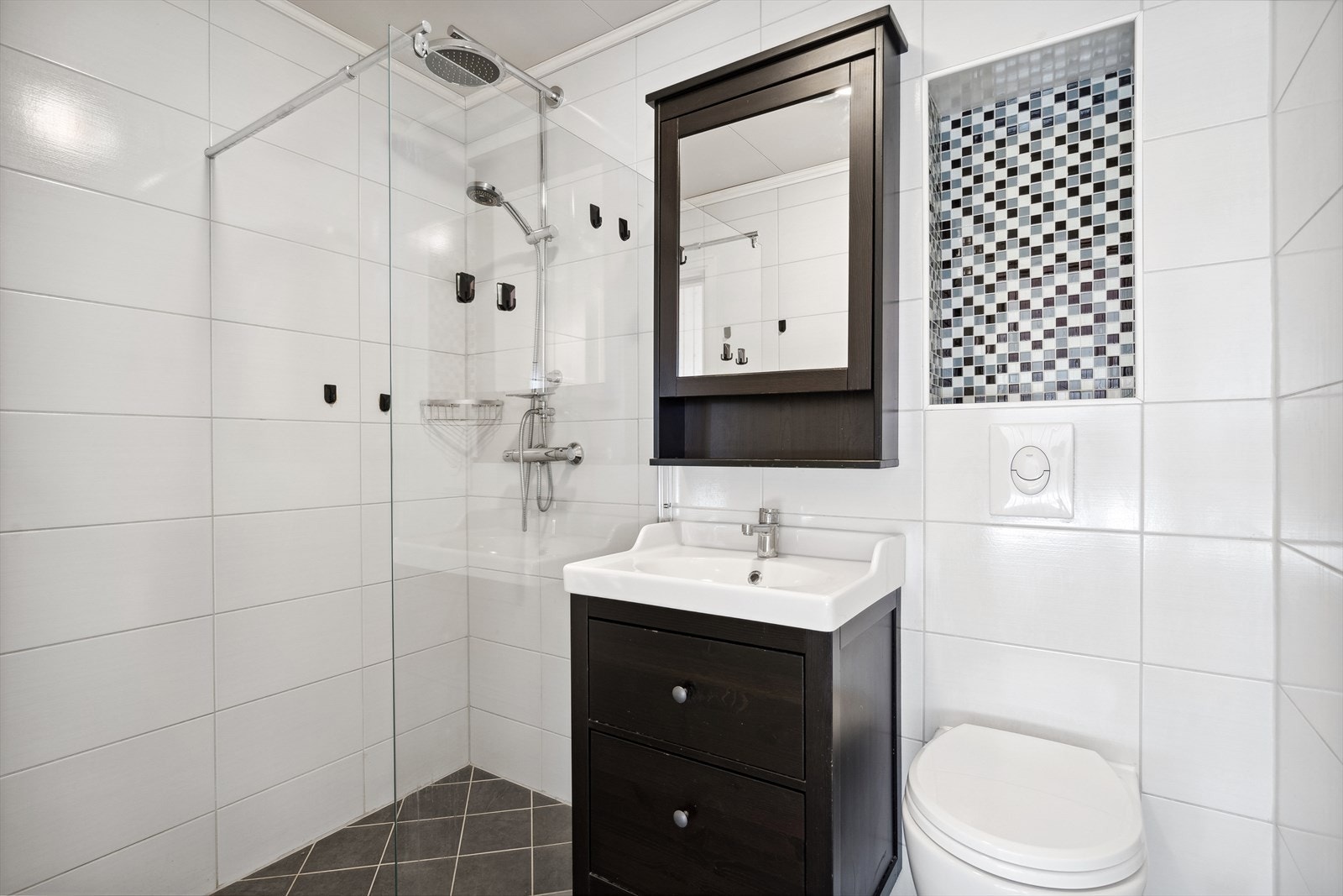 Lyst og fint bad fra 2016 med toalett, dusj og mørk baderomsinnredning. Galleribilde