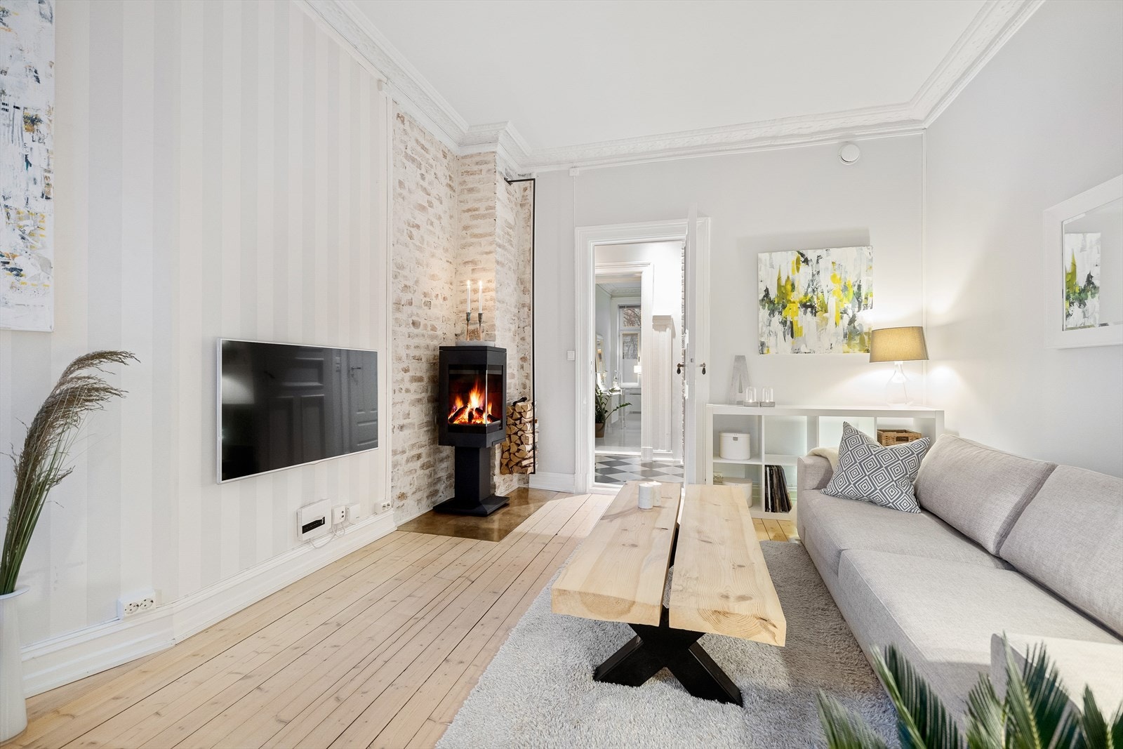 En lys og romslig stue som kombinerer klassiske detaljer som rosett, stukkatur og pene tregulv med rustikk sjarm fra en malt teglsteinsvegg Galleribilde