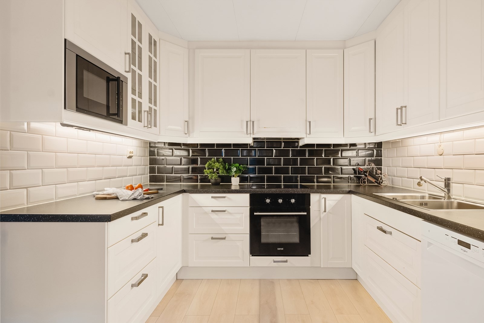 Kjøkkeninnredning med profilerte fronter, laminat benkeplate og fliser over benken. Det er utstyrt med stål oppvaskkum, ventilator og opplegg for oppvaskmaskin Galleribilde