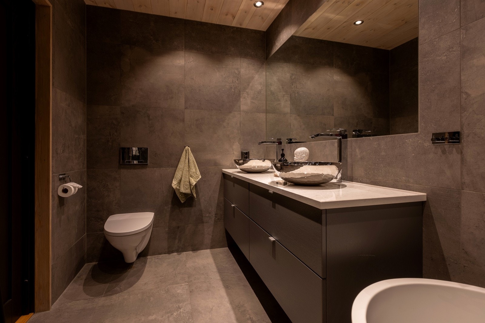 Begge bad er i lik utførelse og har flislagte gulv og vegger og himling med behandlet panel og innfeldte downlights. Galleribilde