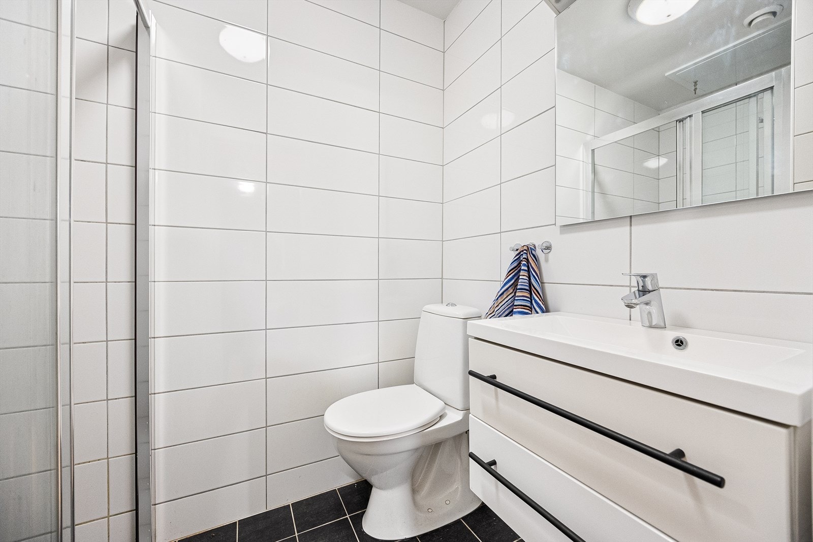Leilighetens bad er helfliset med elektriske varmekabler i gulvet. Badet er innredet med servant med underskap, vegghengt speil, wc, og dusjhjørne. Galleribilde
